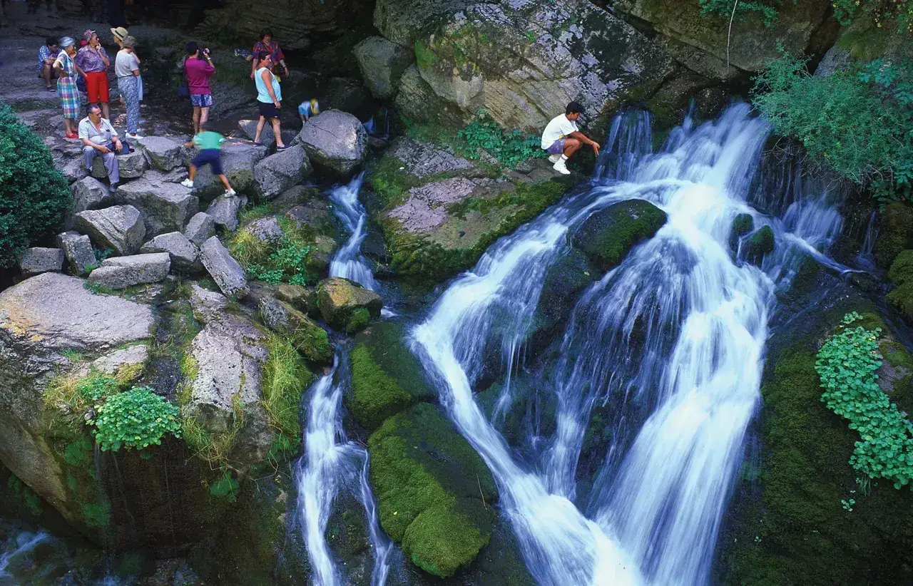 Un joven observa el bullidor de la llet, una cascada de agua cristalina que desciende entre rocas cubiertas de musgo.