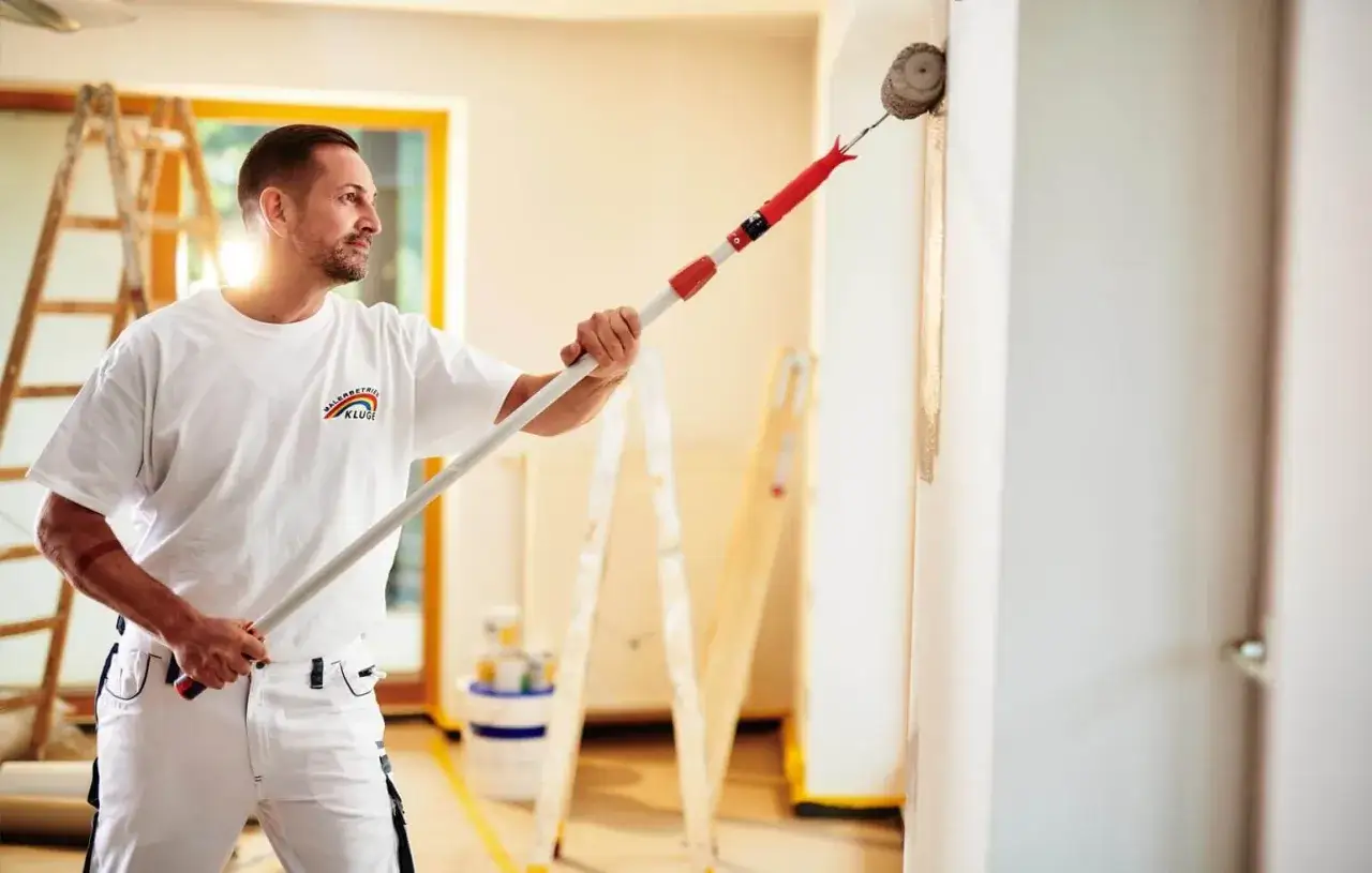 Maler mit Teleskopstange streicht Wand. Informieren Sie sich &uuml;ber die malerarbeiten kosten f&uuml;r Ihr Projekt.