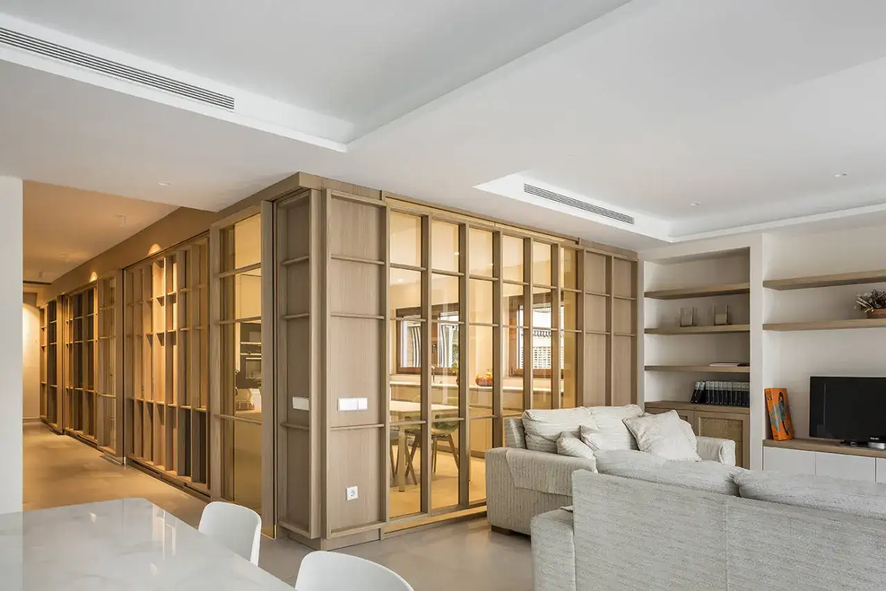 Un dise&ntilde;ador de espacios crea una sala de estar moderna con divisiones de madera y cristal, estanter&iacute;as y sof&aacute;s acogedores.