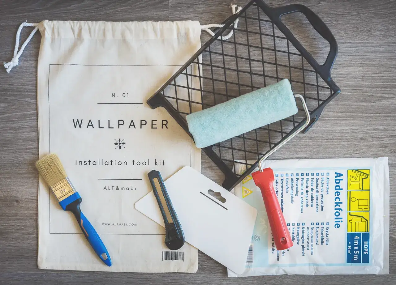 Kit de herramientas para saber como poner papel pintado: brocha, rodillo, cúter y plástico protector.