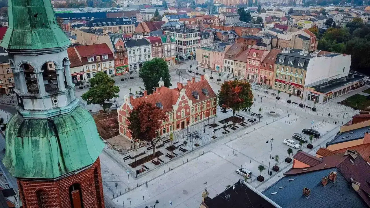 Widok na rynek w Starogardzie Gdańskim, serce Kociewia. Kolorowe kamienice, zabytkowy ratusz i zielona wieża kościelna tworzą malowniczy krajobraz.