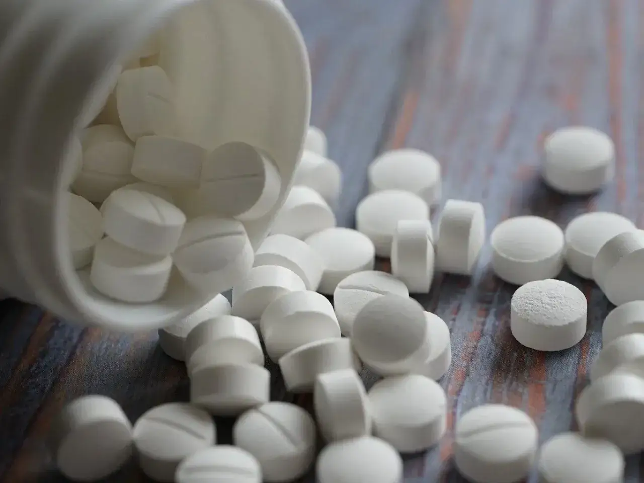 Białe tabletki, jak diazepam bez recepty, rozsypane z białego pojemnika na drewnianym blacie.