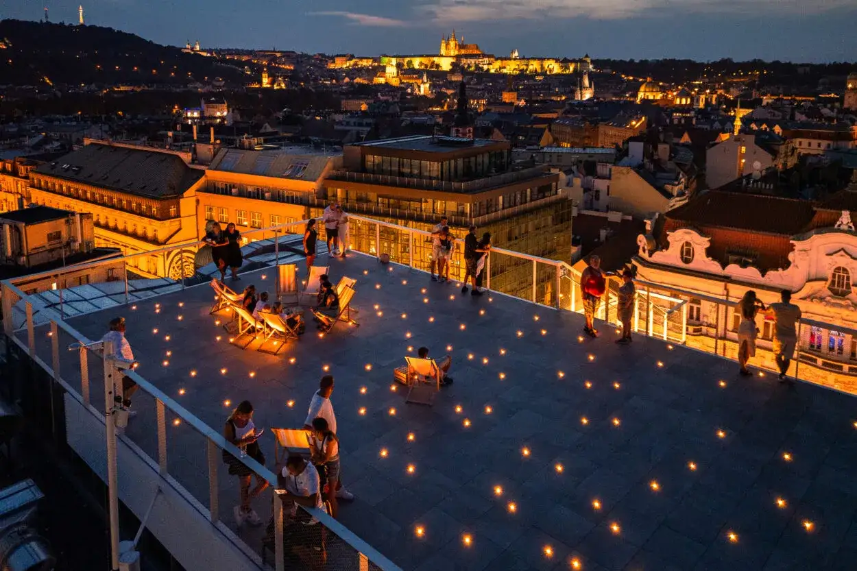 Människor njuter av kvällen på en takterrass med utsikt över upplysta Prag. En perfekt kväll på ett duplex i Prag.