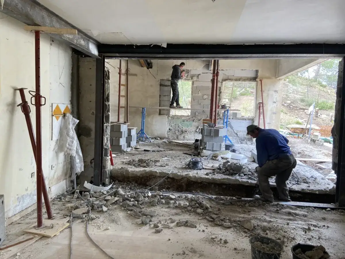 Travaux de démolition en cours pour une aide à la rénovation maison ancienne. Des ouvriers utilisent des outils pour casser le béton.
