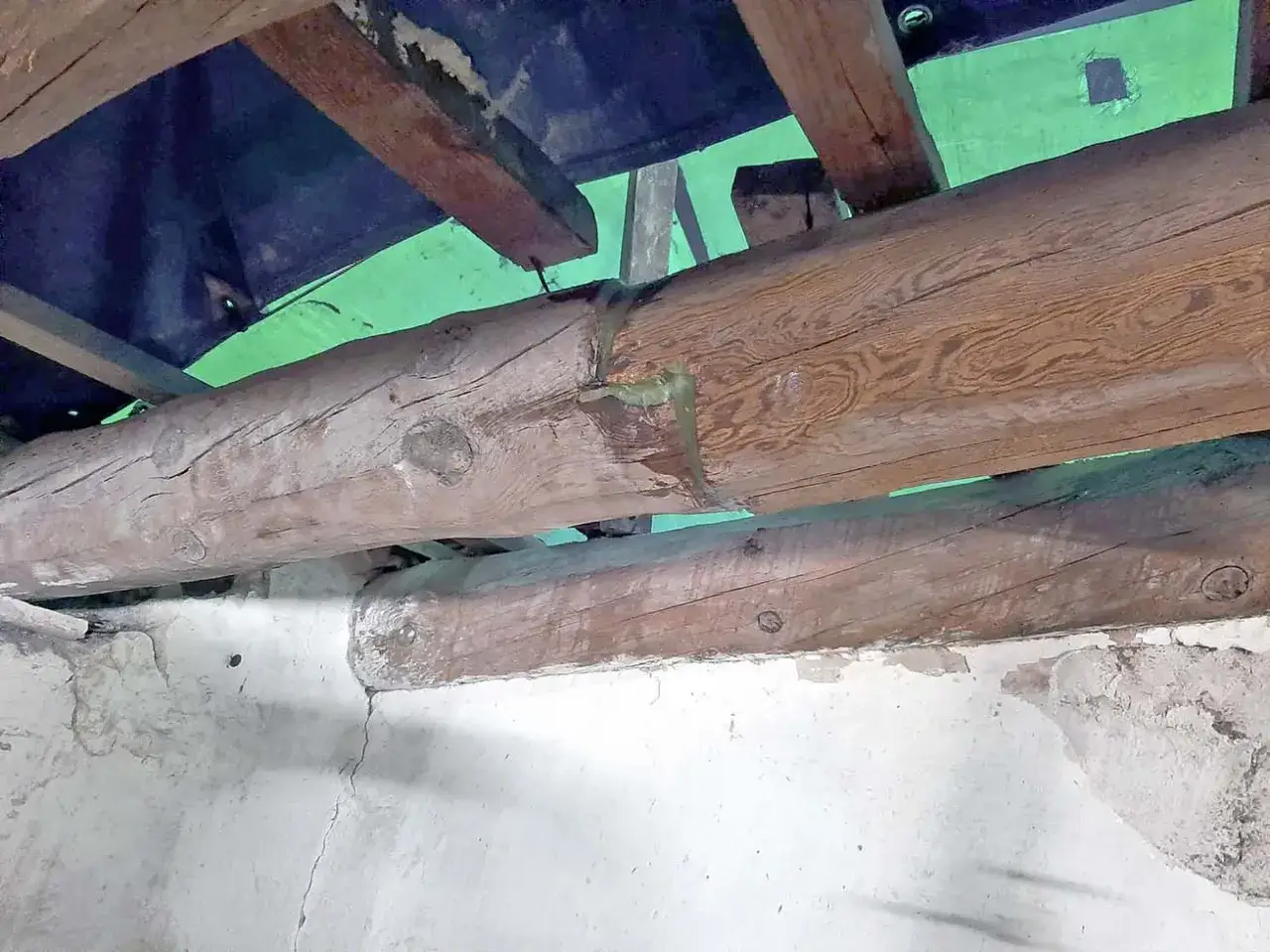 Detalle de cómo reforzar una viga de madera con una resina verde, mostrando la viga principal y otra inferior apoyada en una pared de mampostería.