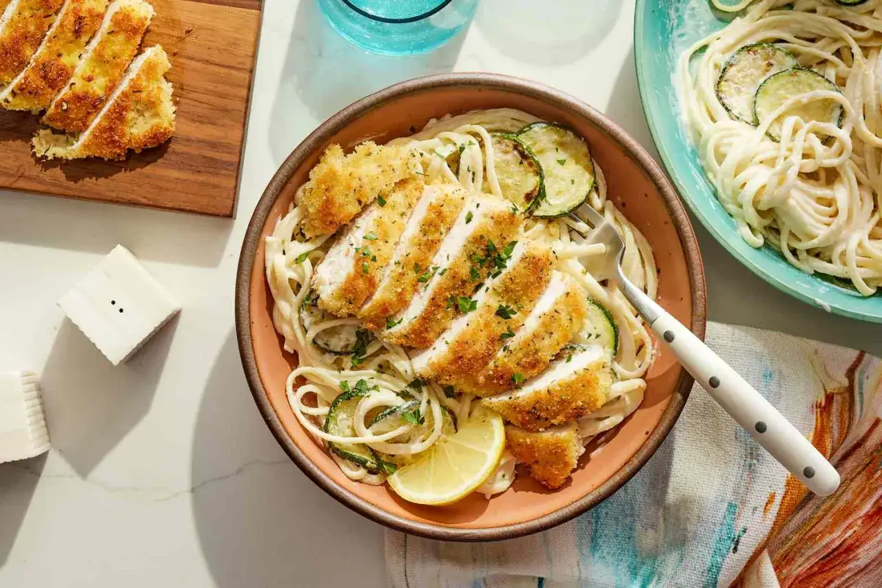 En sk&aring;l med kr&auml;mig citronpasta med kyckling, toppad med krispiga kycklingfil&eacute;er och zucchini. En citronskiva ger extra fr&auml;sch&ouml;r.