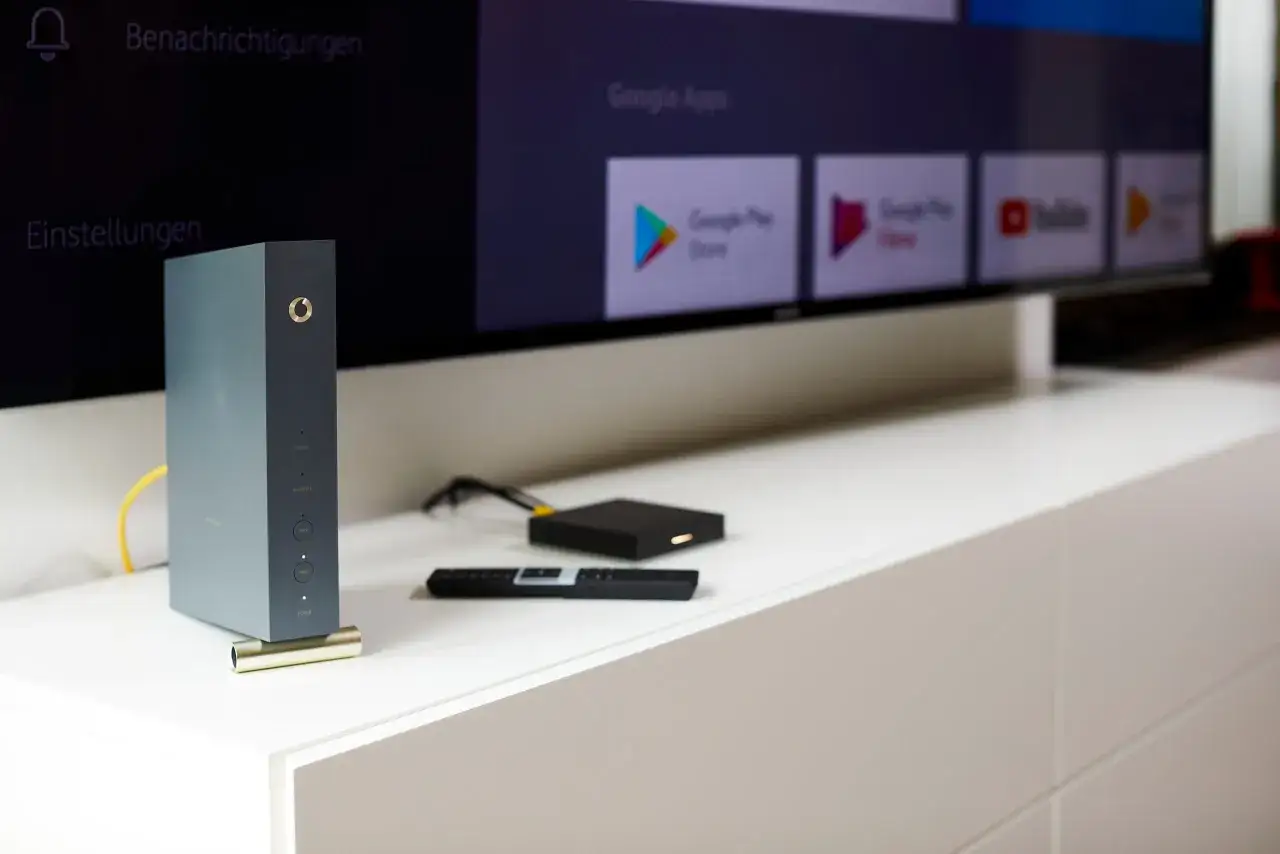 Vodafone Station mit WiFi 6, daneben ein Media-Receiver und eine Fernbedienung vor einem Smart-TV.