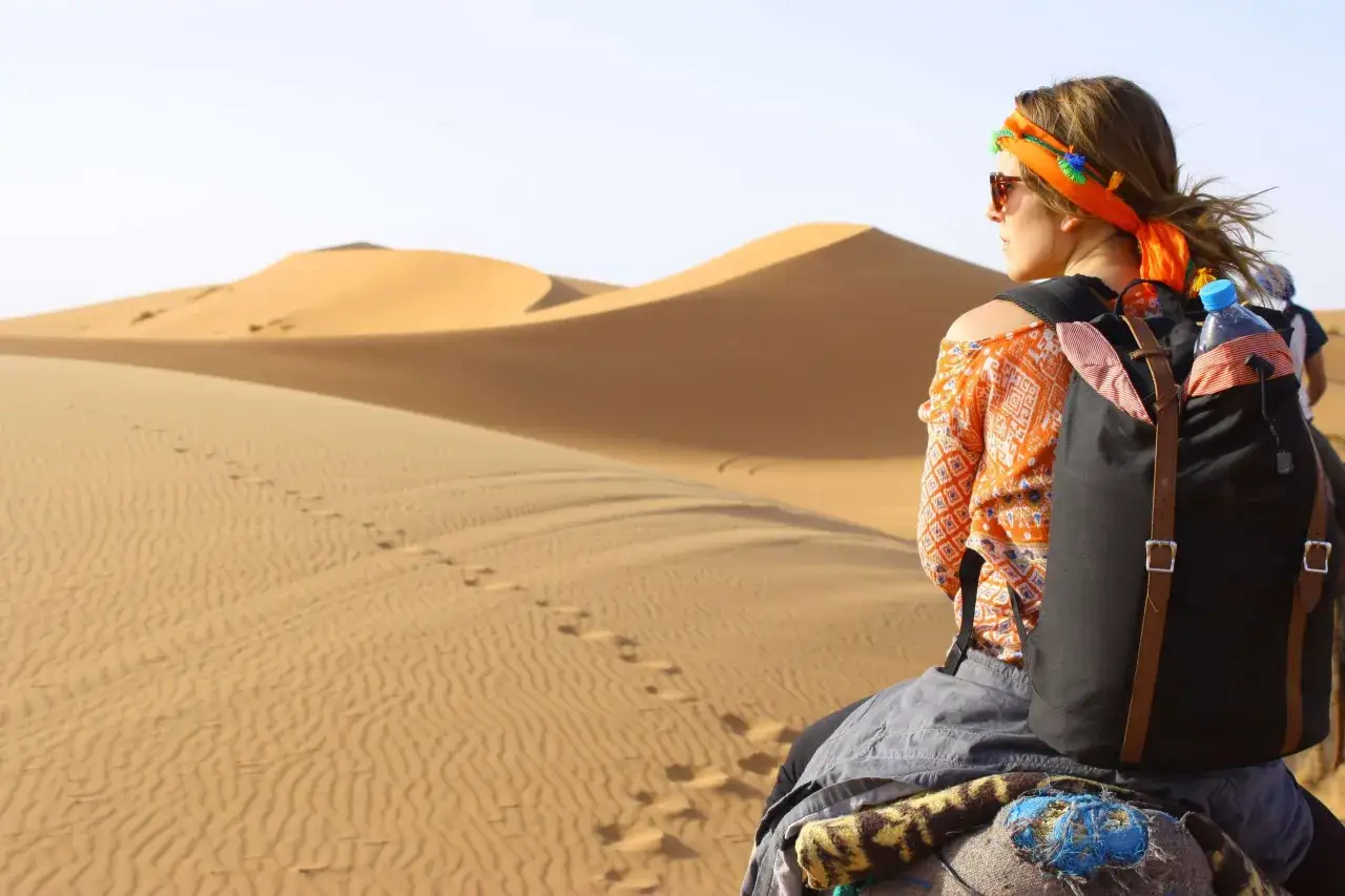 Une femme profite d'un trek dans le d&eacute;sert, observant les dunes de sable ondulantes sous un ciel clair.