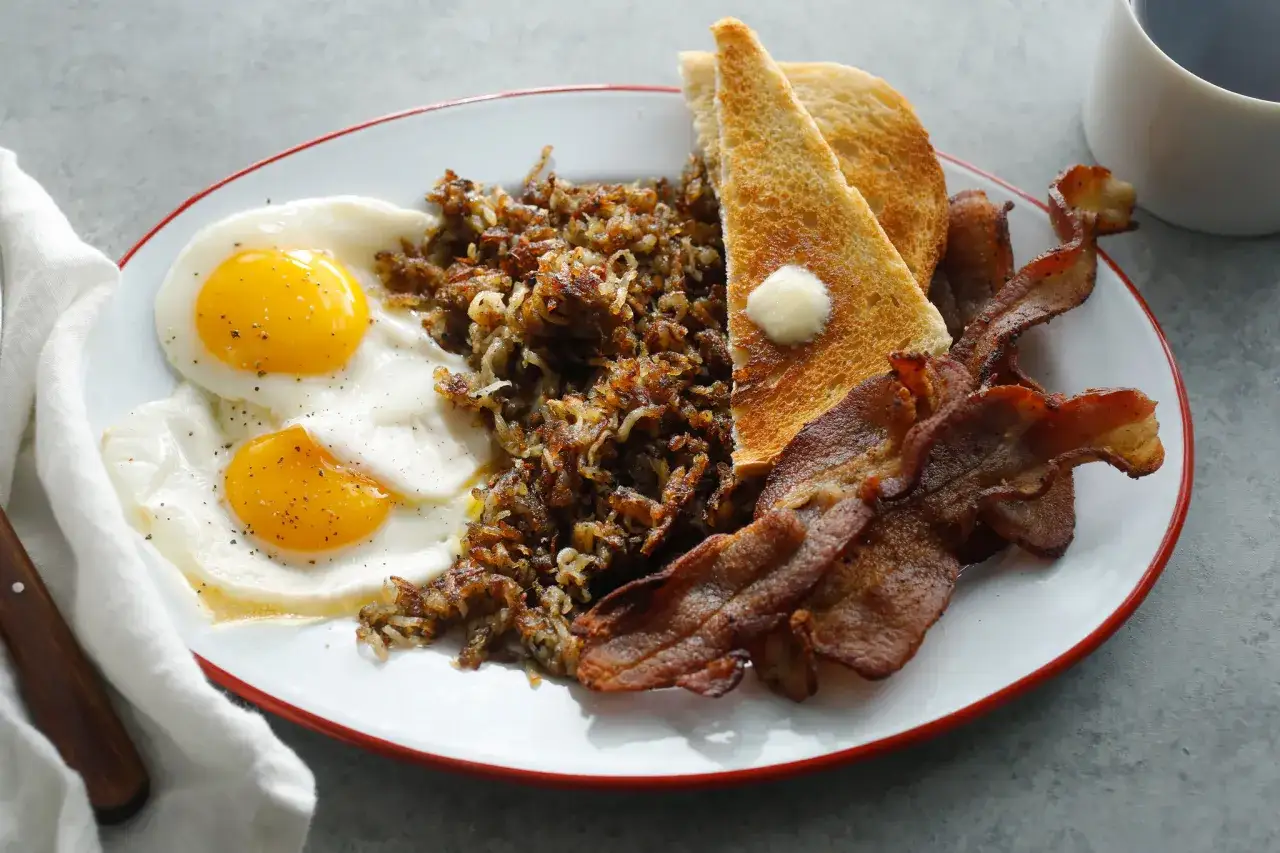 Typowe amerykańskie śniadanie: jajka sadzone, chrupiący bekon, ziemniaki hash browns i tosty z masłem.