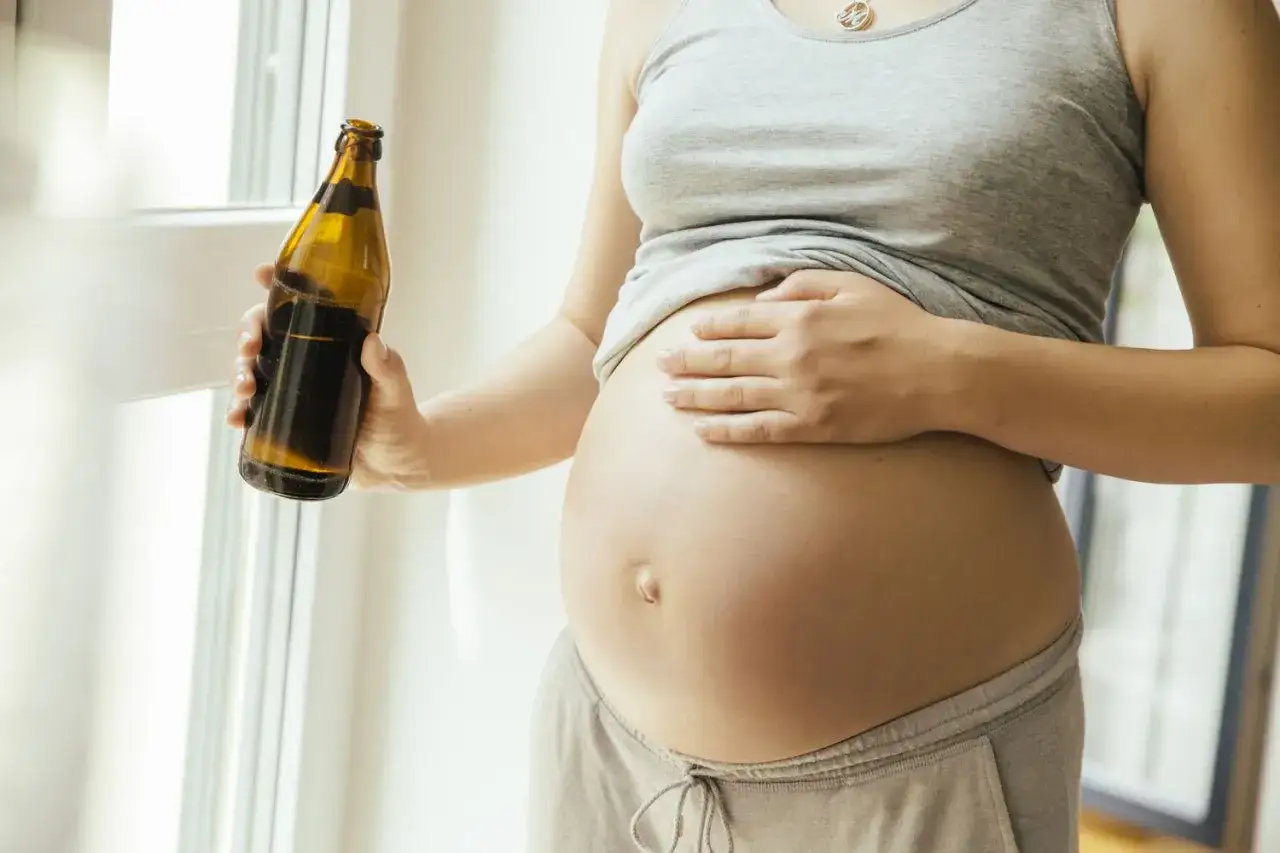 Schwangere Frau hält Flasche mit dunklem Getränk. Vielleicht ein alkoholfreies Bier oder tonic water schwangerschaft?