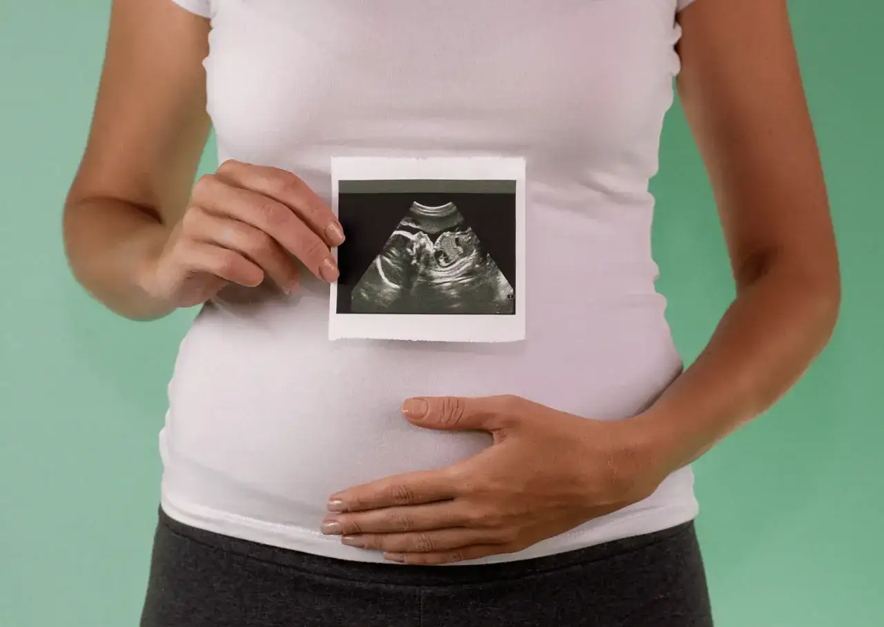 Ultraschallbild eines Babys, das in der 18. SSW geboren wurde, gehalten vor dem Bauch einer werdenden Mutter.