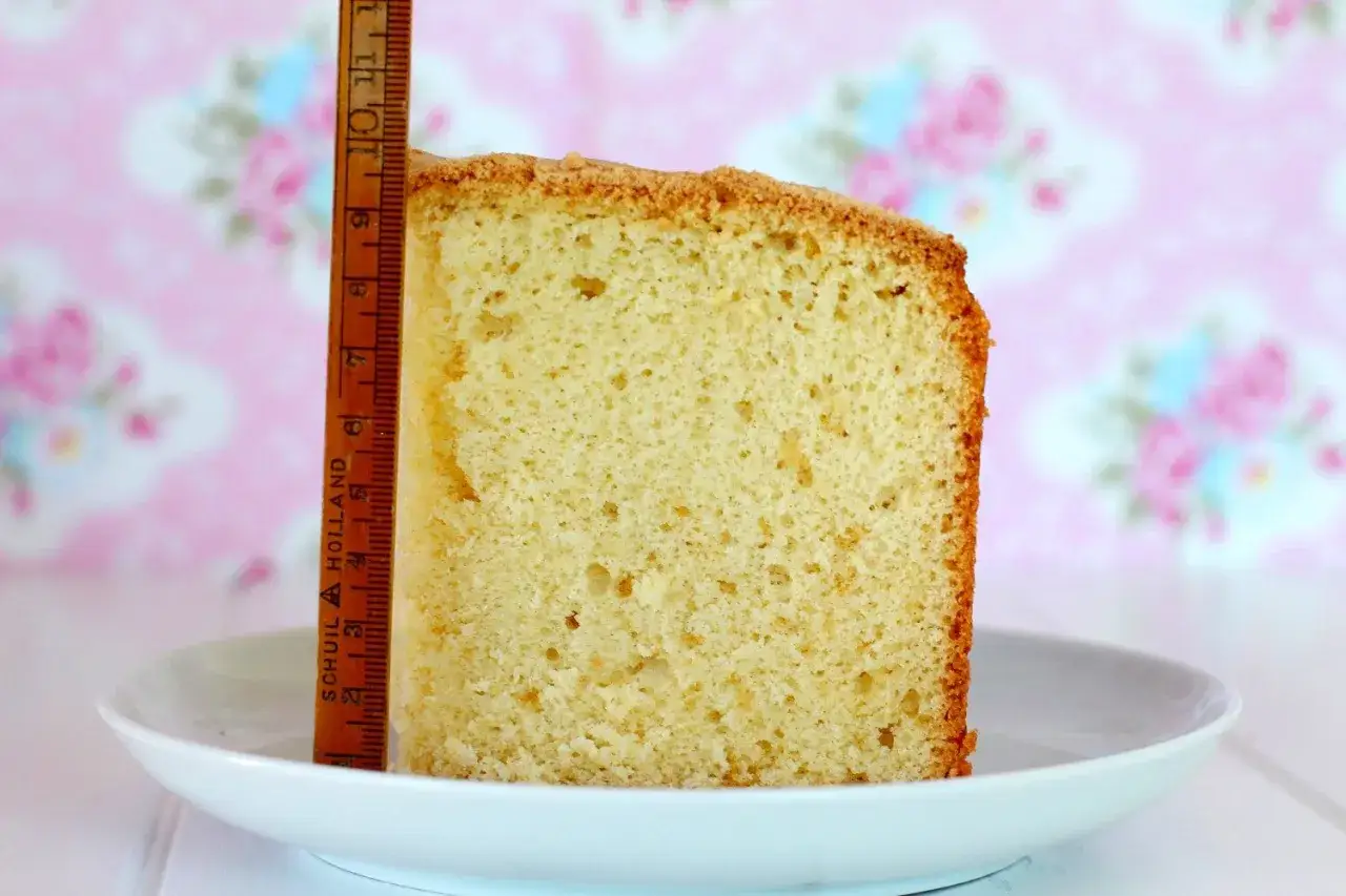 Rebanada de bizcocho esponjoso, como una harp sponge, junto a una regla de madera. Fondo rosa con flores.