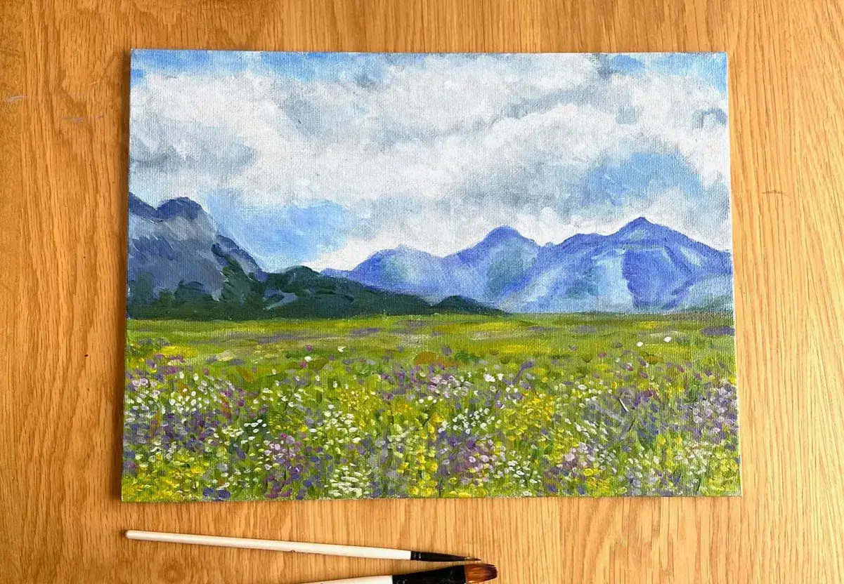 Peinture paysage facile débutant : un champ de fleurs sauvages multicolores sous un ciel nuageux, avec des montagnes bleues en arrière-plan.