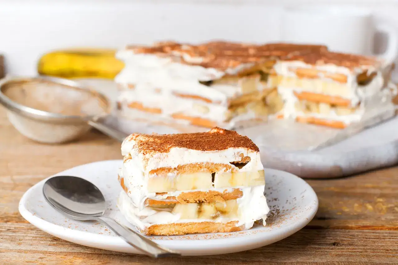 Ein Stück Bananen Tiramisu mit Schichten aus Keksen, Sahne und Bananen, bestäubt mit Kakaopulver.