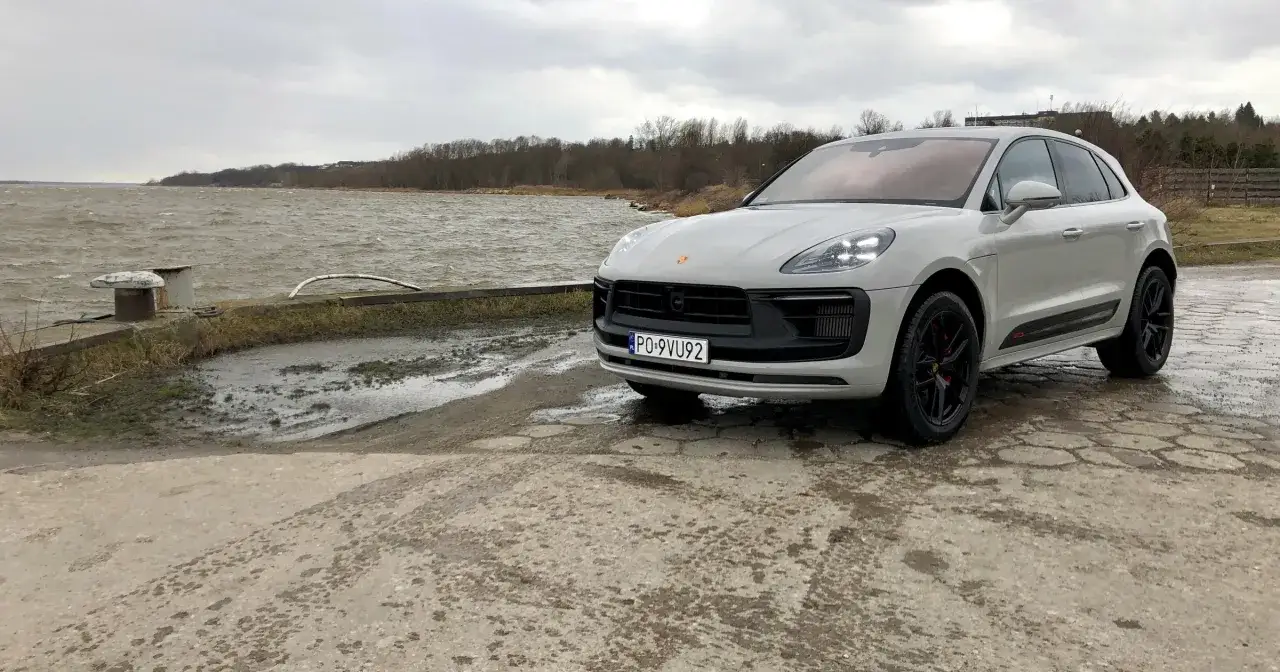 Szary Porsche Macan GTS z czarnymi felgami stoi nad wzburzoną wodą.