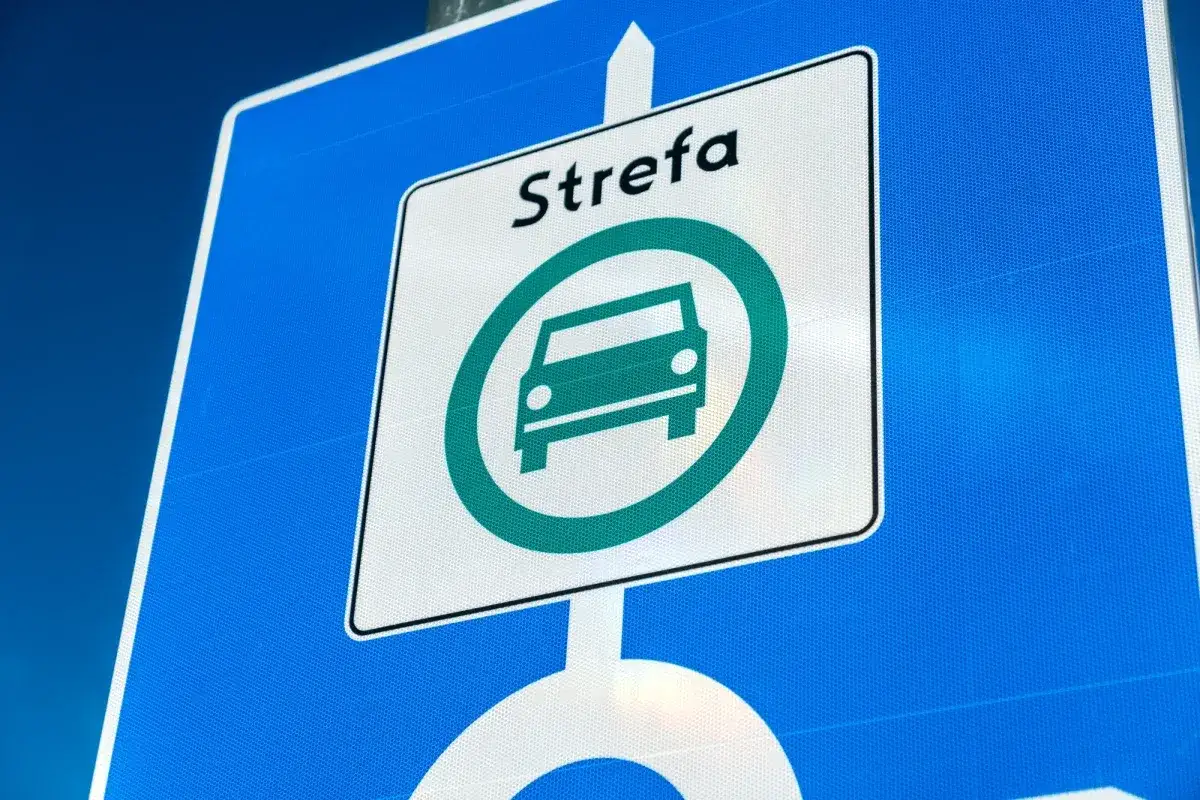 Znak informuje o wjeździe do strefy czystego transportu. Zielony symbol samochodu w okręgu oznacza ograniczenia dla pojazdów spalinowych.