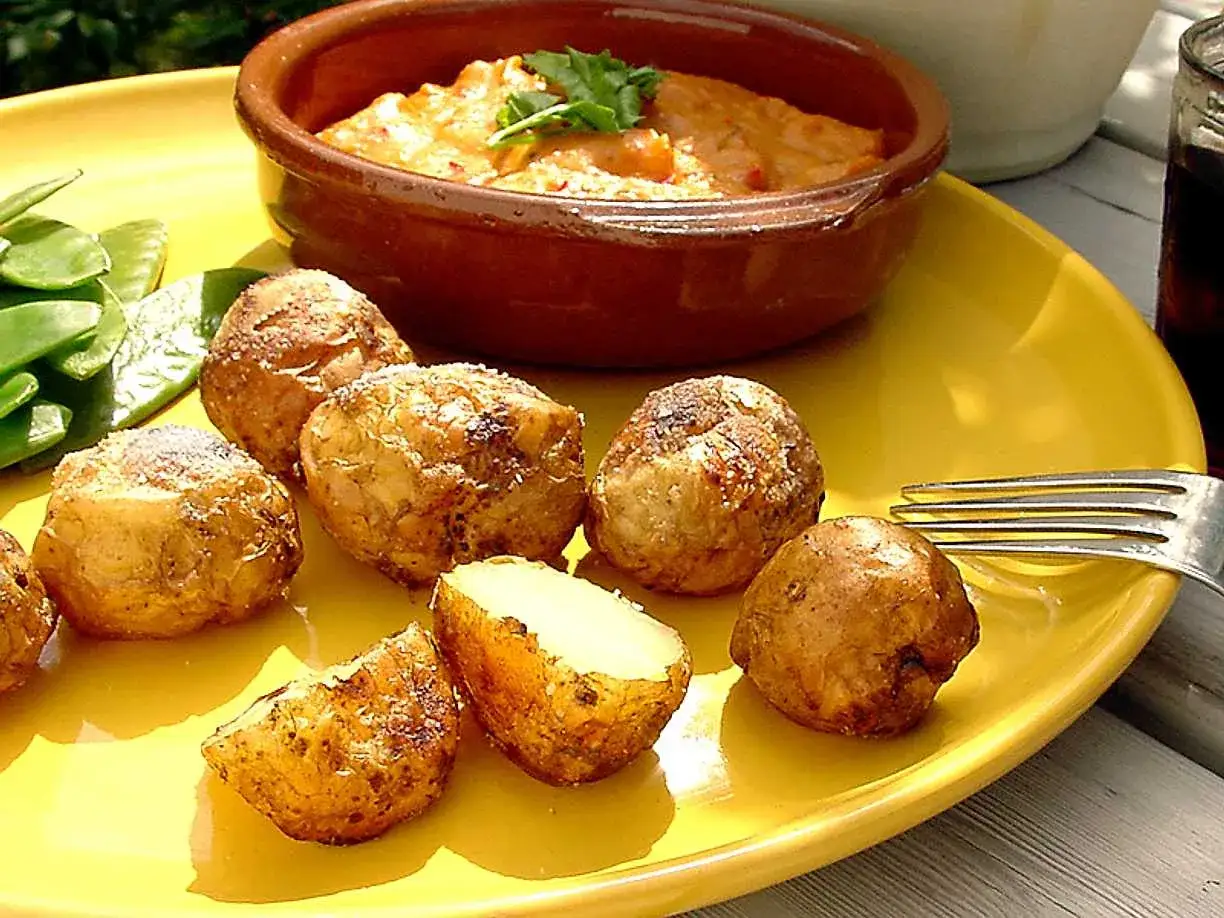 Sm&aring;, skrynkliga papas arrugadas med en mustig s&aring;s och gr&ouml;na b&ouml;nor p&aring; en gul tallrik.
