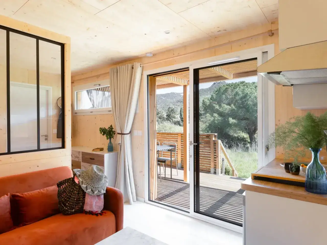 Am&eacute;nagement petit studio cosy avec canap&eacute; orange, cuisine fonctionnelle et vue sur la nature.