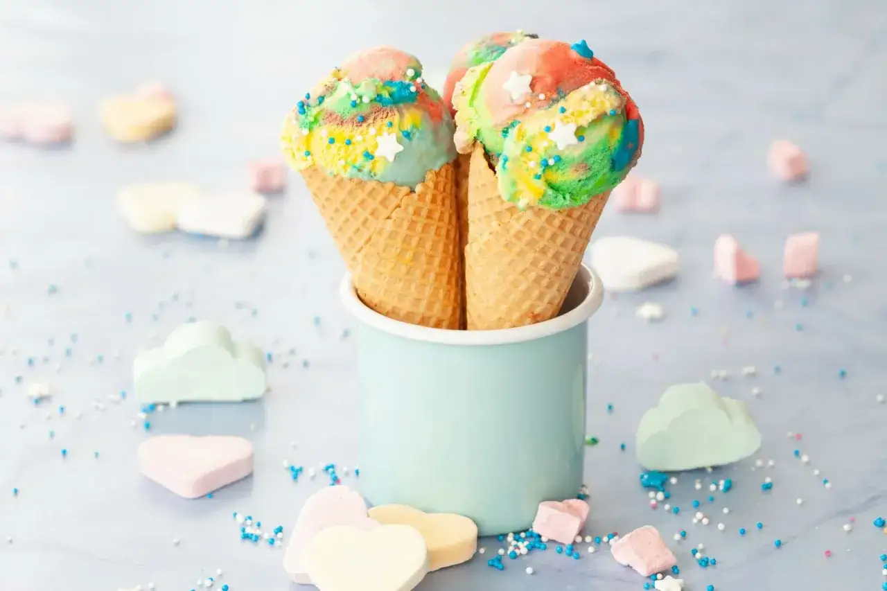 Zwei Waffelh&ouml;rnchen mit buntem regenbogen eis, bestreut mit bunten Streuseln und Sternen.