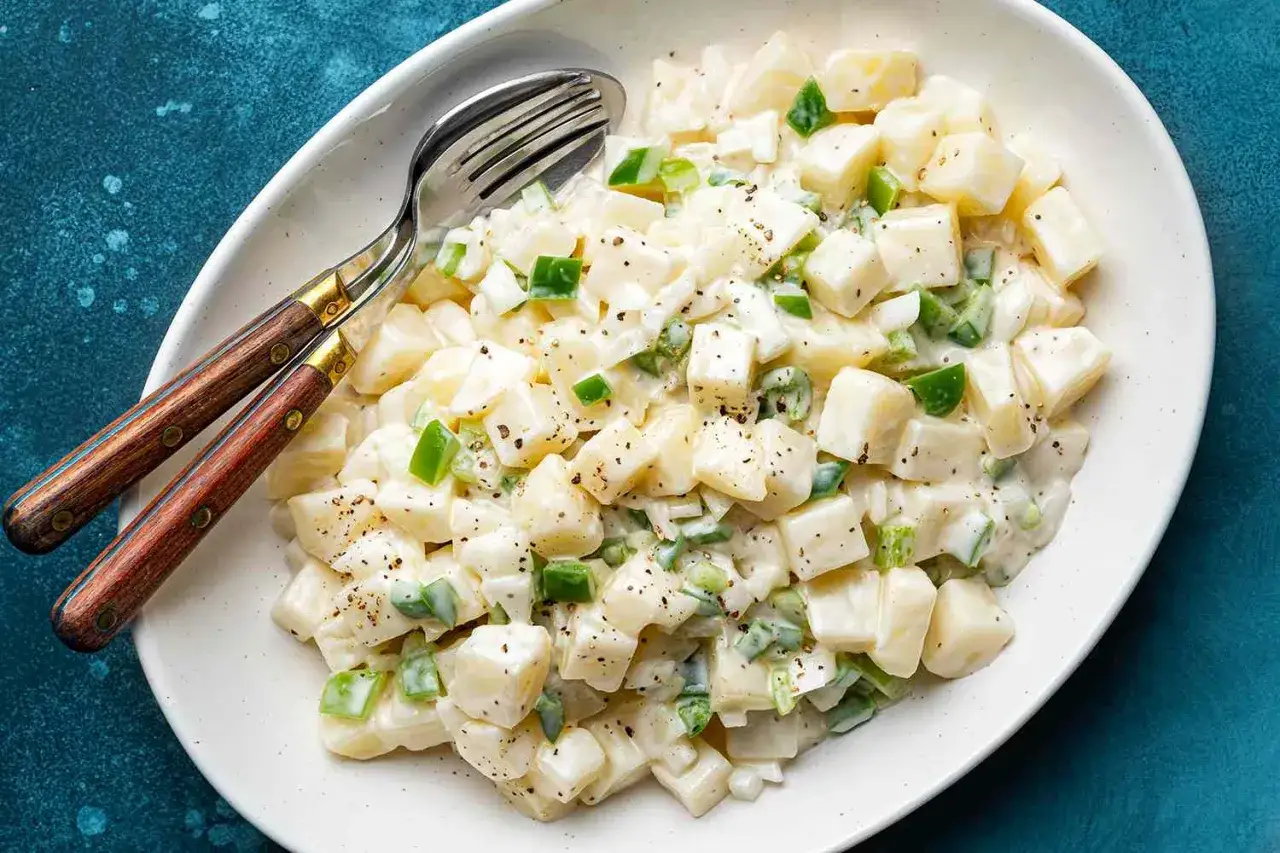 Cremiger Kartoffelsalat mit grünen Paprikawürfeln und einem köstlichen Kartoffel Dressing, serviert mit Besteck.