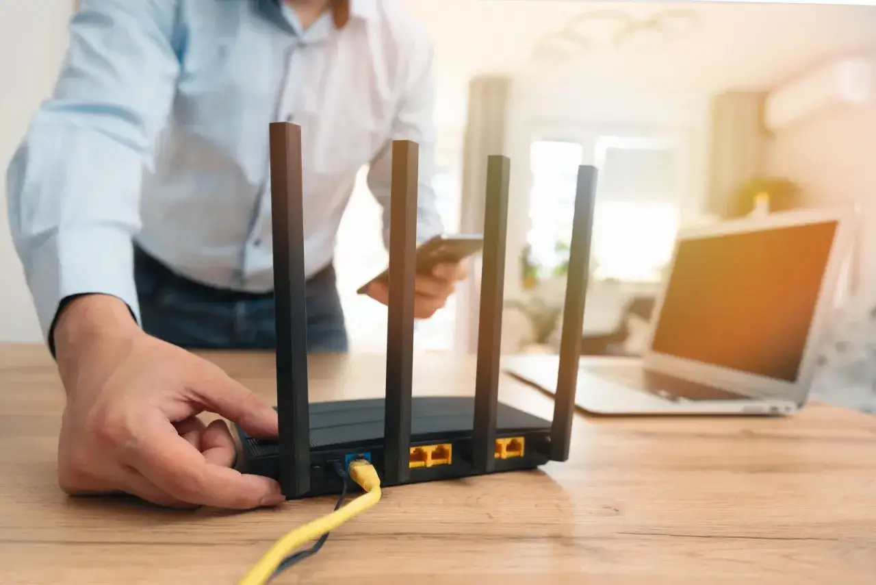 Człowiek sprawdza router, zastanawiając się, dlaczego internet wolno chodzi. W tle widać laptopa.