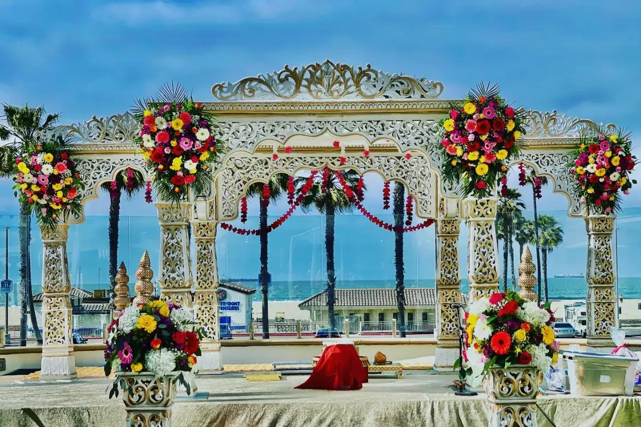 Prachtvoller Mandap für eine Bollywood-Hochzeit am Strand, geschmückt mit bunten Blumen und Palmen im Hintergrund.