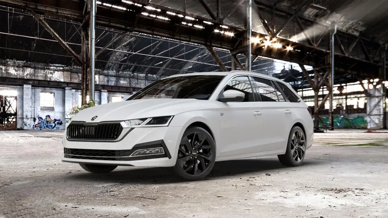 Biała Skoda Rapid Combi z czarnymi felgami, prezentująca różne rozmiary opon, stoi w opuszczonej hali przemysłowej.
