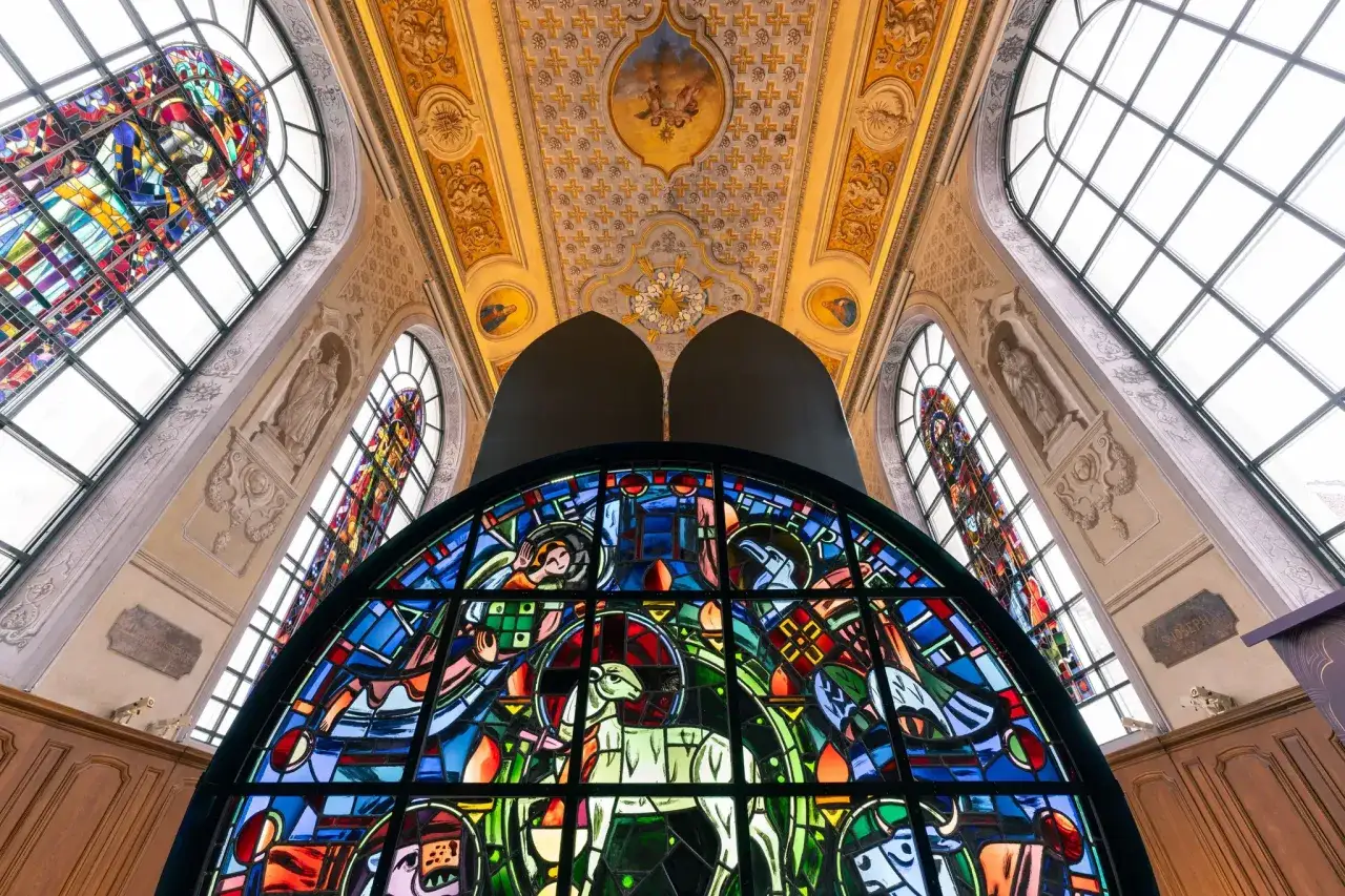 Vitraux de Notre Dame, un agneau blanc au centre d'une scène colorée, baignant la pièce de lumière.