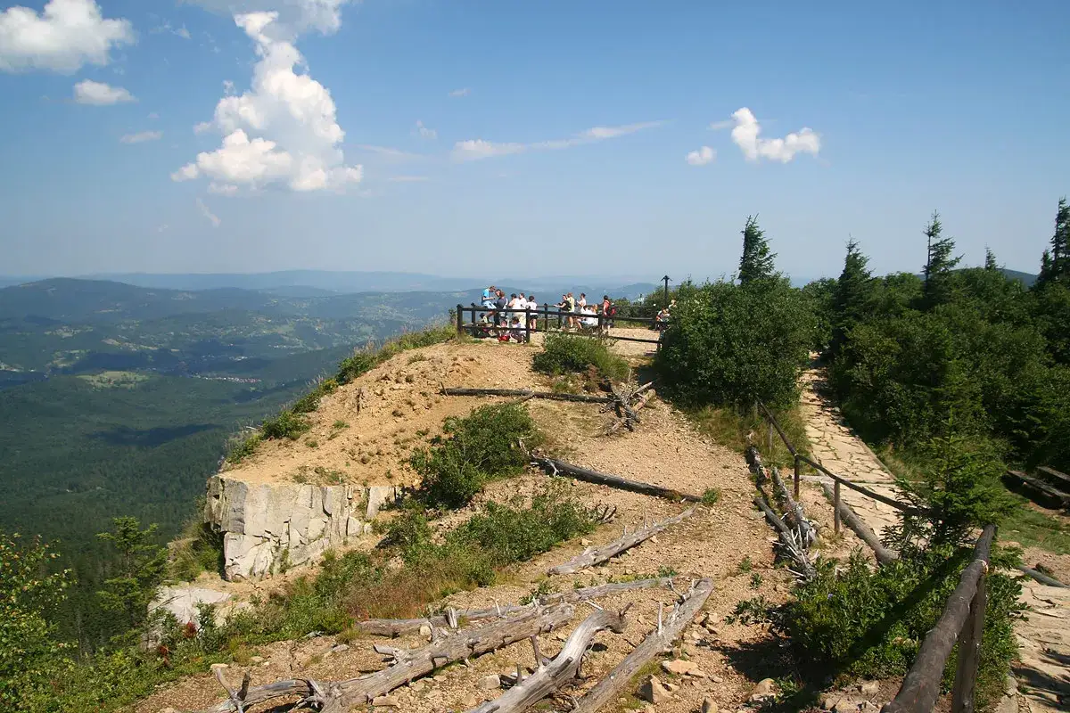 Widok z sokolicy na Babiej G&oacute;rze. Grupa turyst&oacute;w podziwia panoramę Beskid&oacute;w.