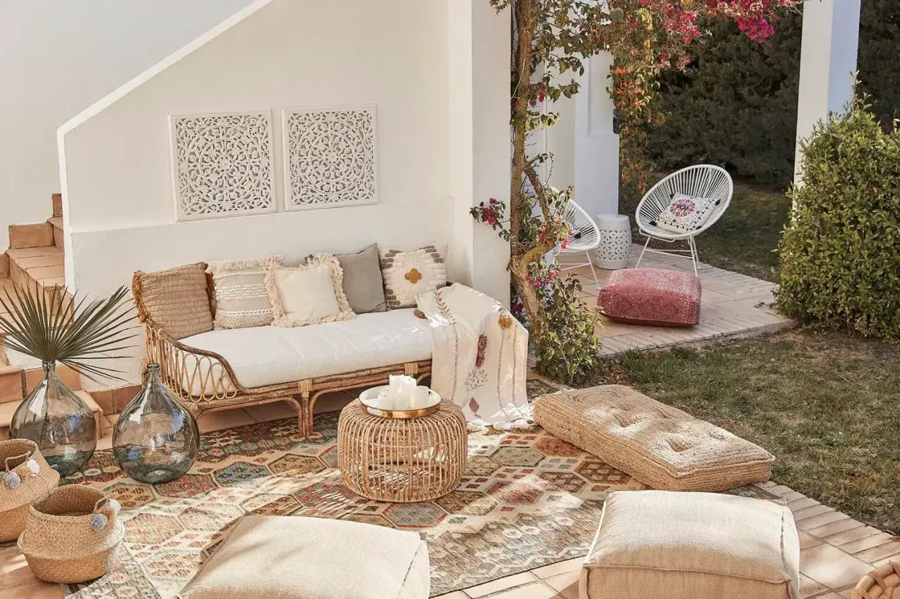 Acogedor patio andaluz moderno con sof&aacute; de rat&aacute;n, alfombra colorida y cojines. Un oasis de relax bajo la buganvilla.