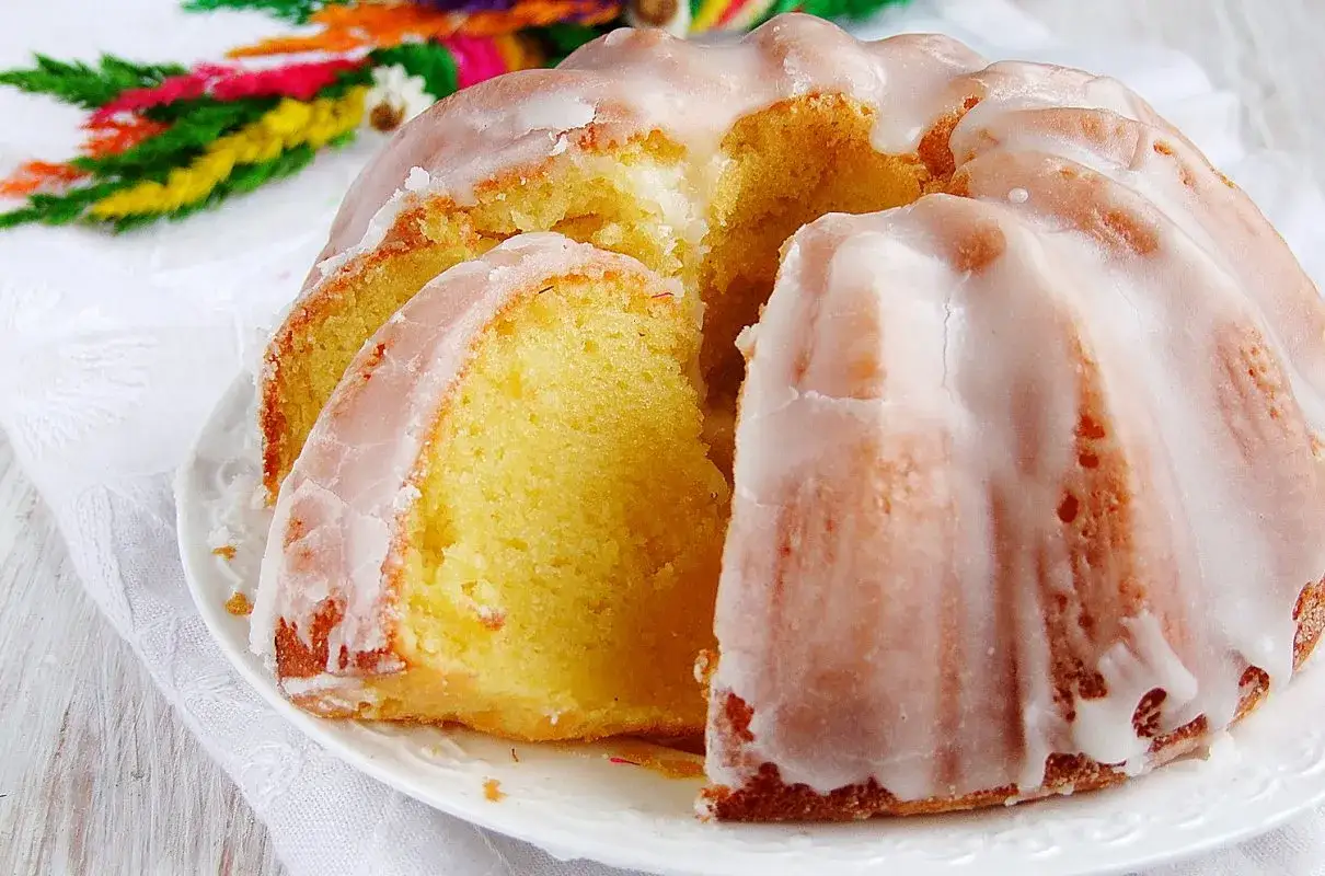 Szybka babka wilgotna, polana lukrem, z widocznym kawałkiem ciasta. W tle kolorowe palemki.