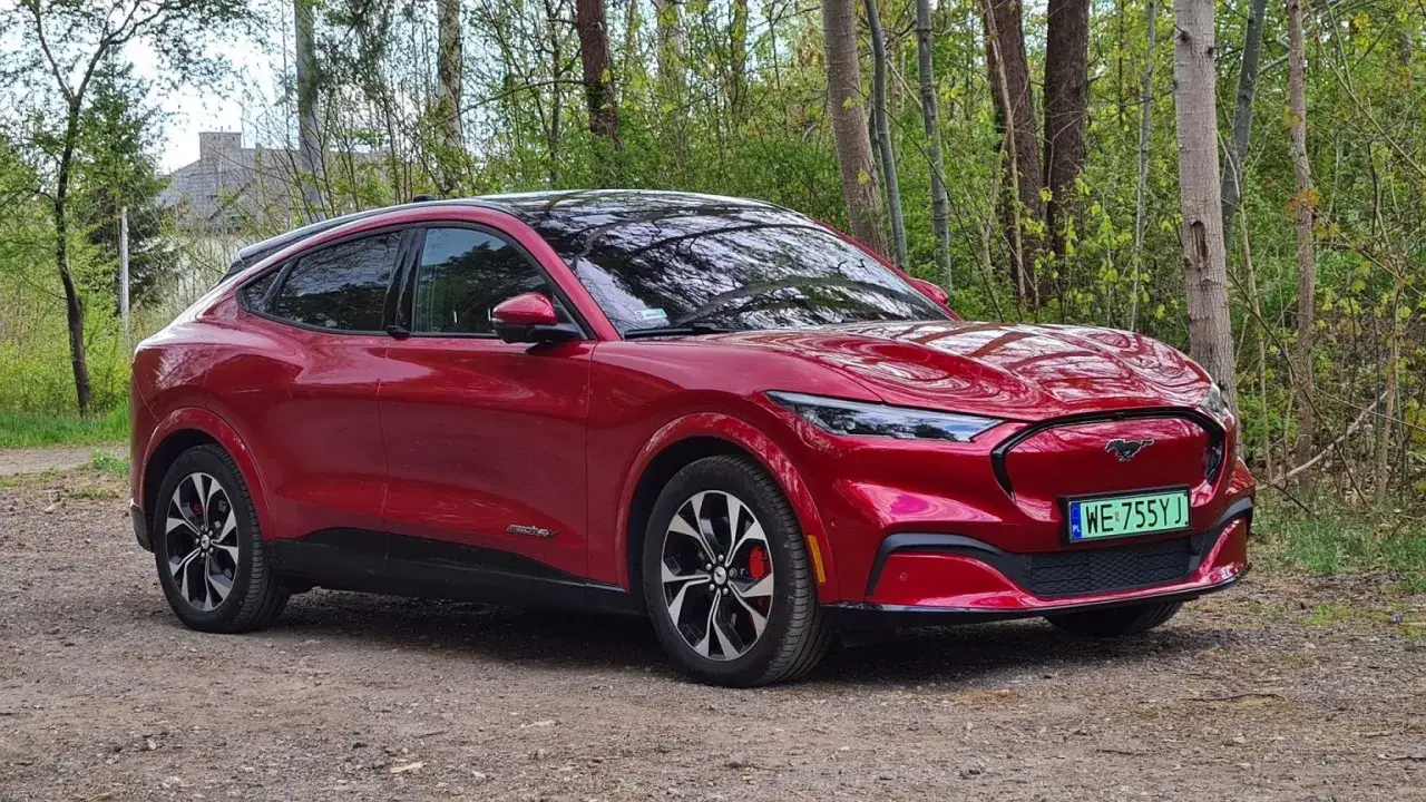 Czerwony Mustang Mach-E na leśnej drodze. Ten elektryczny SUV oferuje imponujący zasięg, idealny na długie podróże.