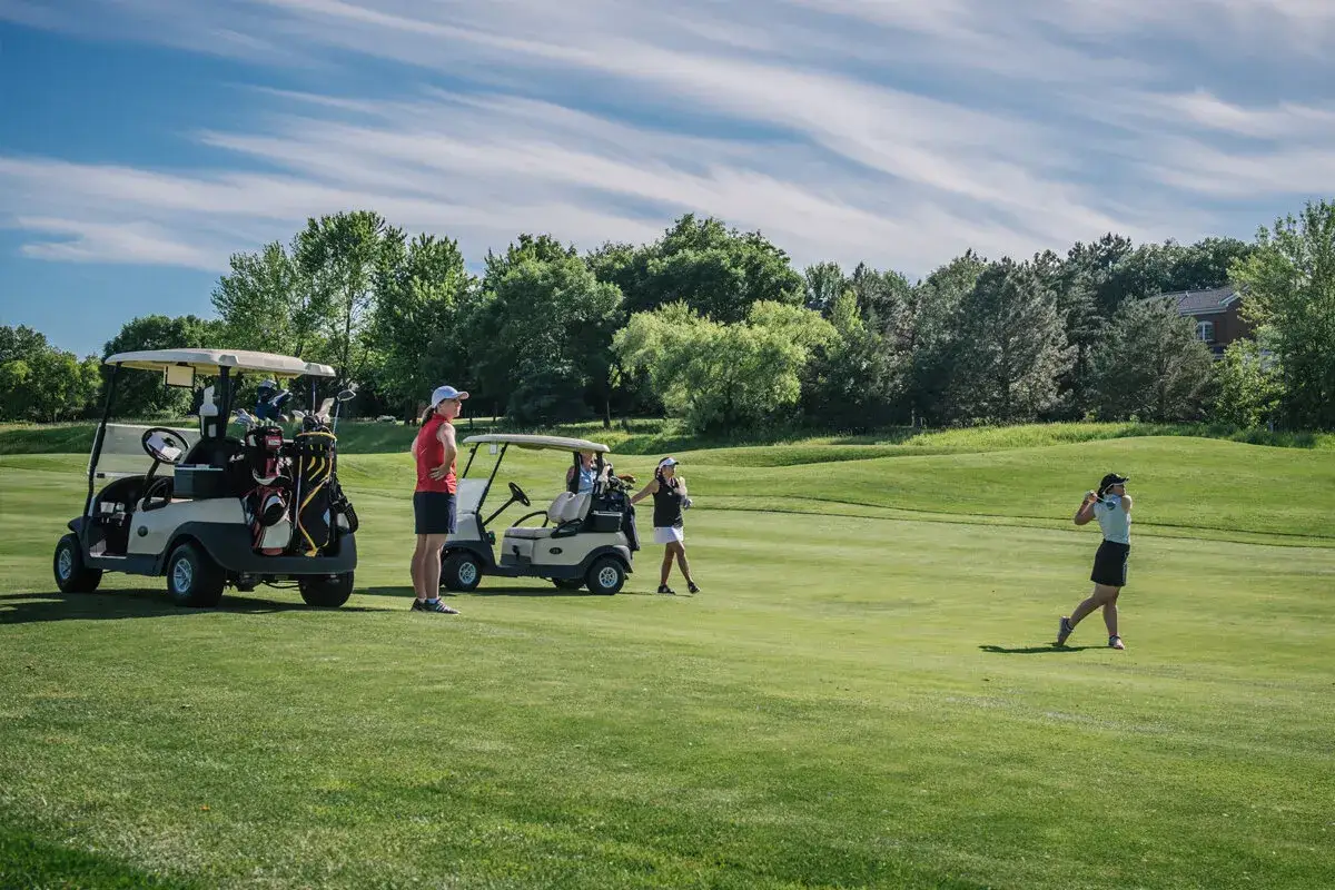 Women golfers on a sunny course, with carts and clubs ready. This scene inspires great golf tournament fundraiser ideas for a fun day out.