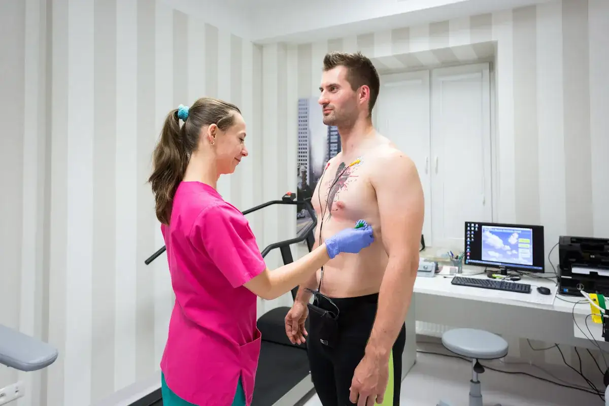Pielęgniarka zakłada elektrody do badania EKG. Pacjent ma podłączony holter, kt&oacute;ry monitoruje pracę serca przez 24h, pomagając ocenić, jak spać z holterem.