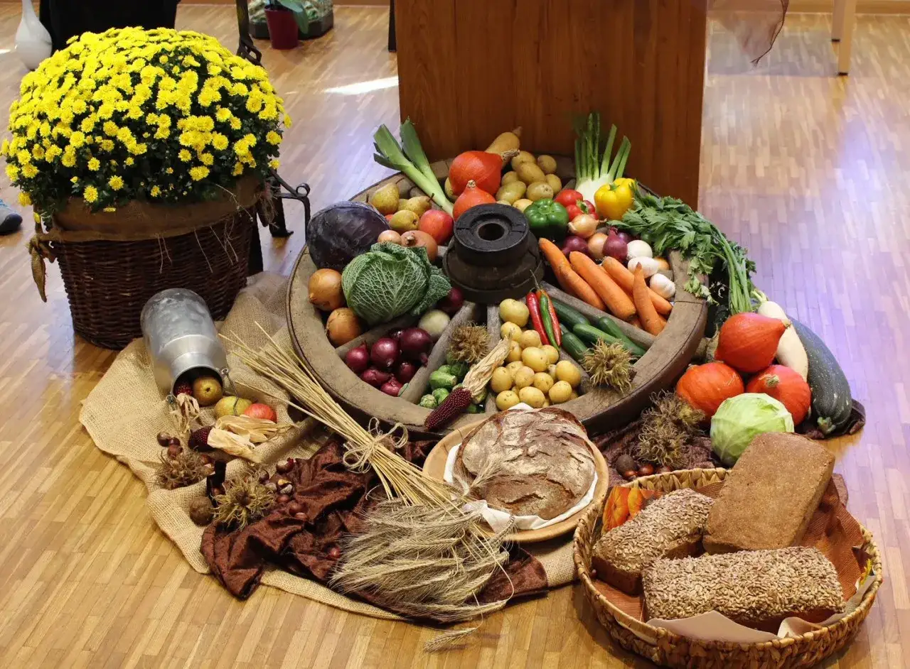 Ein Rad mit Gem&uuml;se und Fr&uuml;chten, um einen Erntedankaltar zu gestalten. Gelbe Chrysanthemen und Brot vervollst&auml;ndigen die Szene.