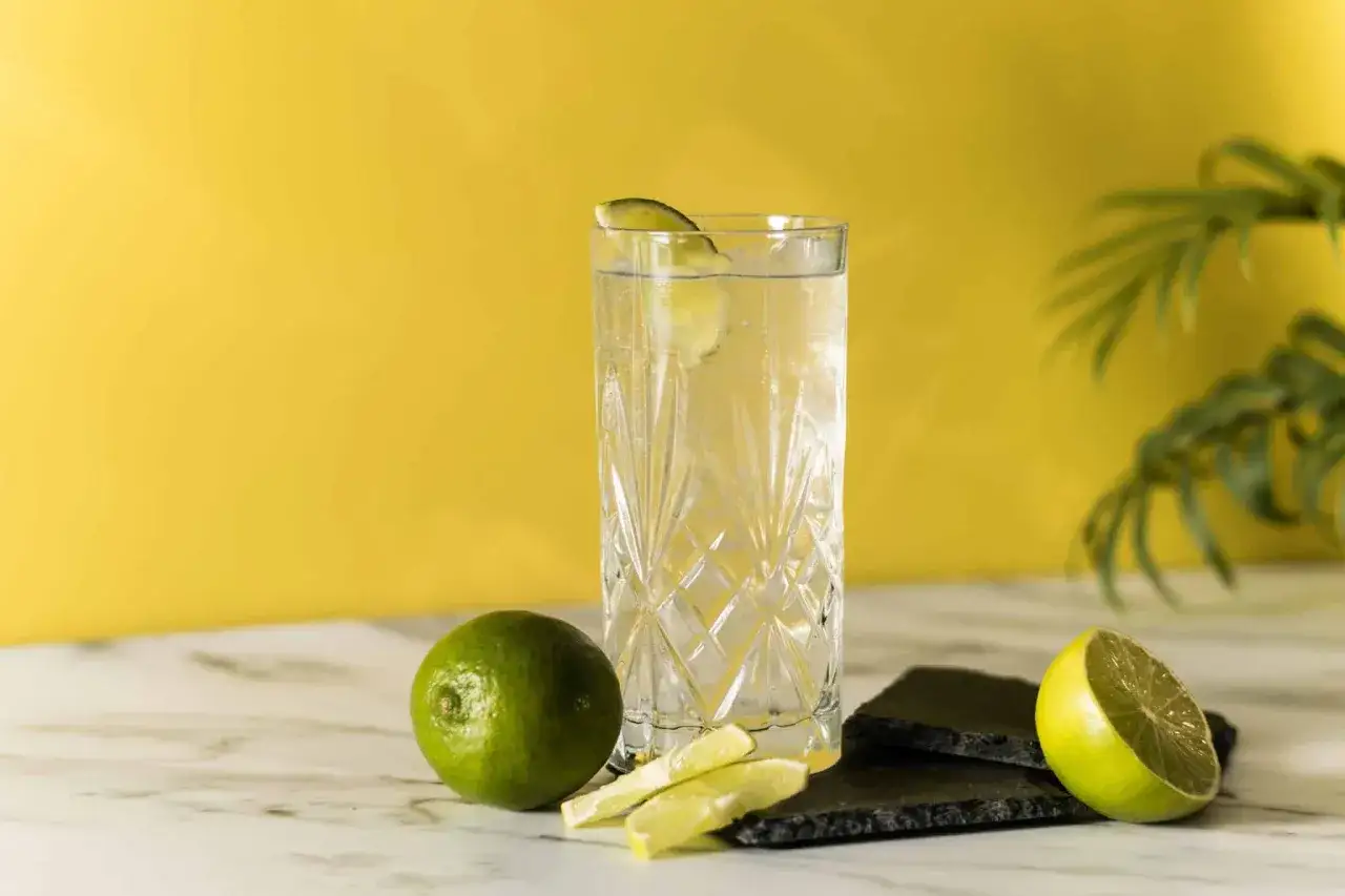 Orzeźwiająca wódka z tonikiem, ozdobiona plasterkiem limonki, obok świeżych owoców. Idealna na letnie popołudnie.