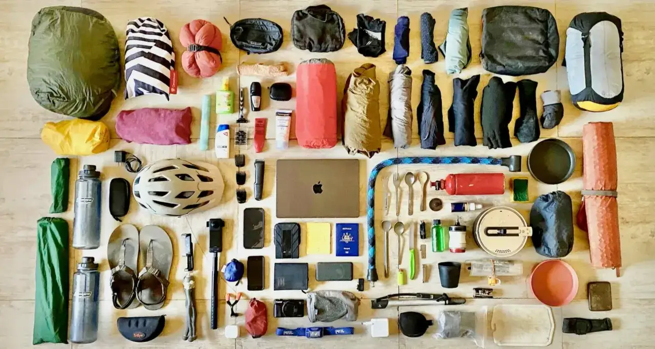 Rozłożony niezbędnik rowerzysty: śpiwór, namiot, kask, bidony, narzędzia, laptop, odzież i akcesoria podróżne.