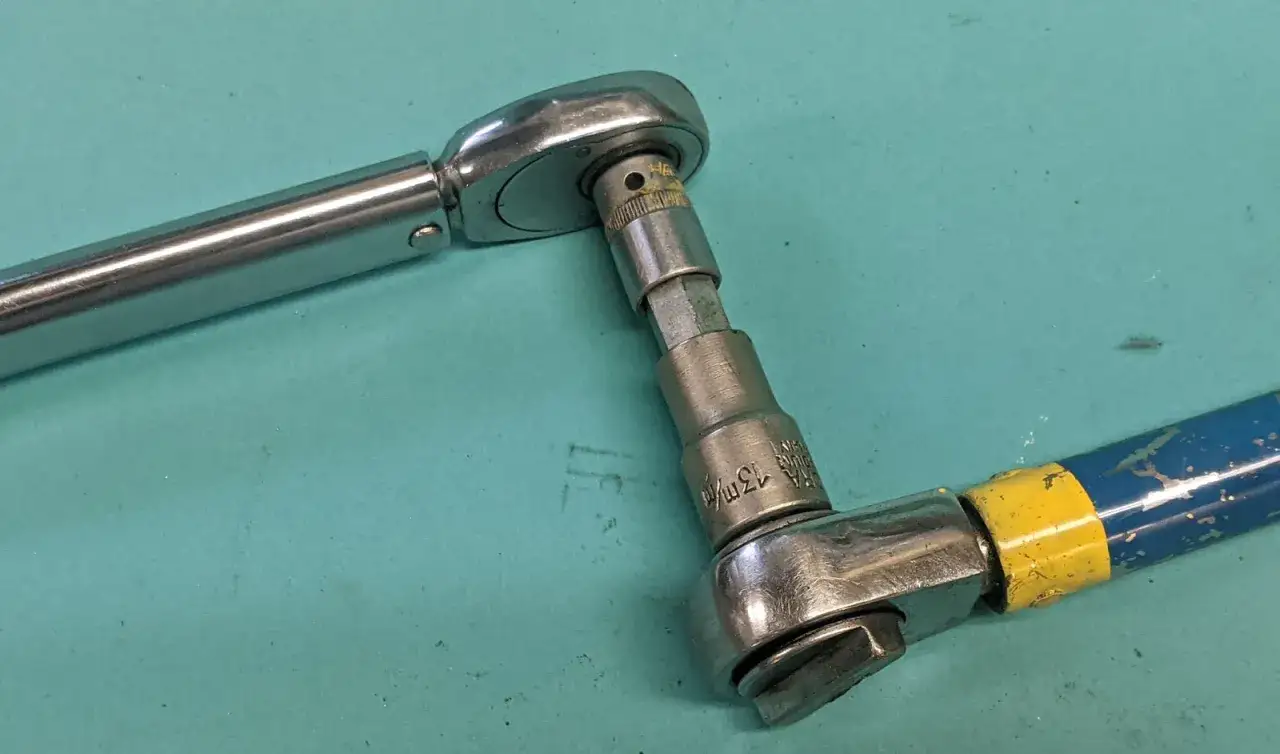 Tv&aring; verktyg kopplade f&ouml;r att kalibrera momentnyckel. En momentnyckel i metall kopplad till en hylsa med en bl&aring; och gul handtagsf&ouml;rl&auml;ngning.
