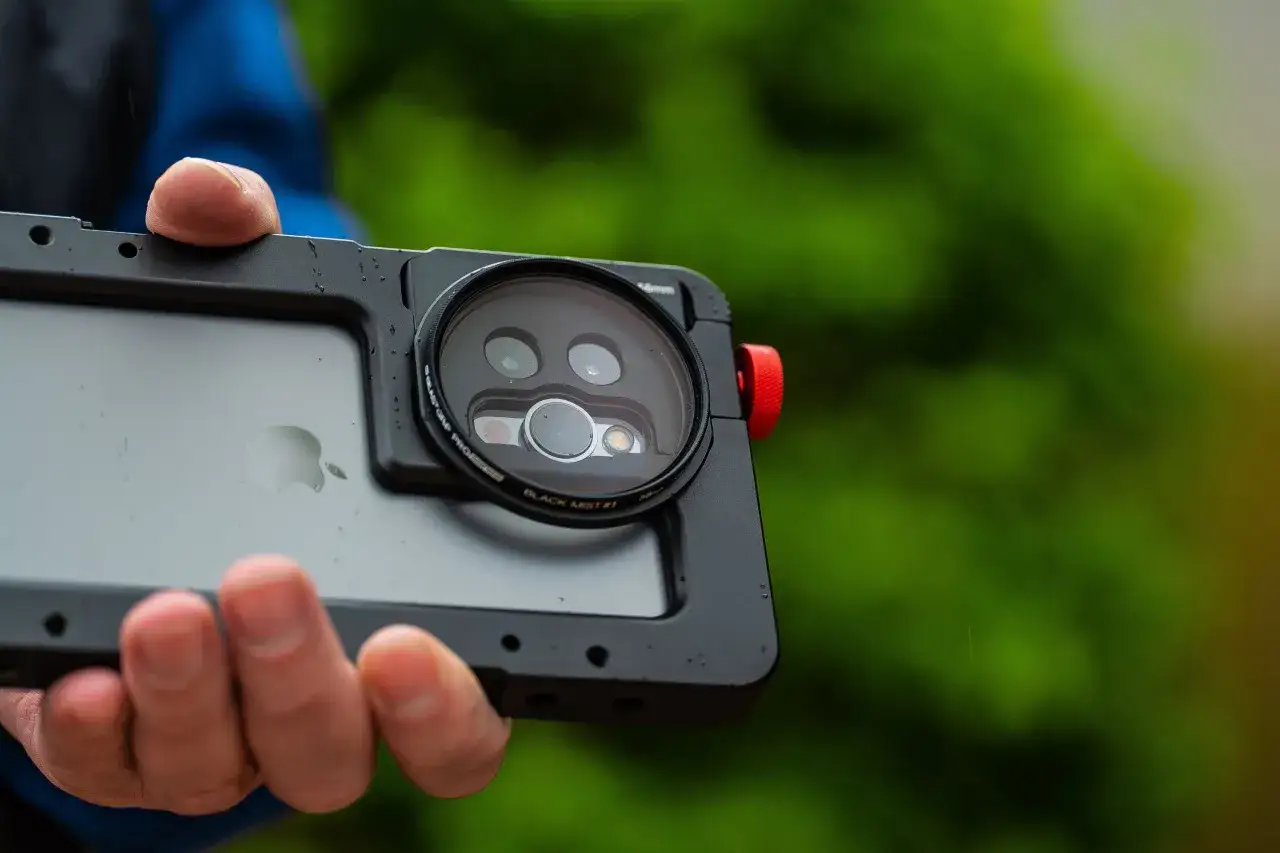 Dłoń trzyma iPhone 13 w obudowie z filtrem na aparat.