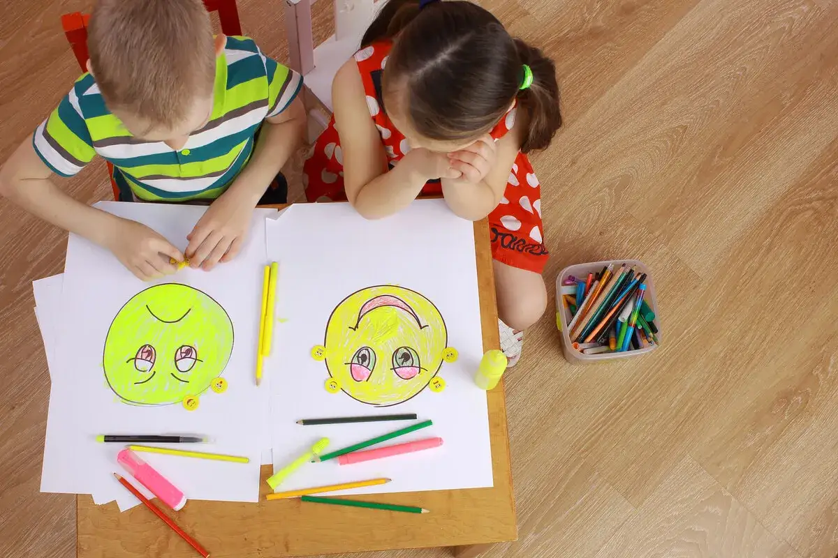 Niños dibujando caras sonrientes y tristes en una actividad para trabajar la empatía.