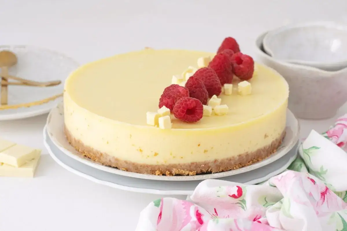 Deliciosa tarta de chocolate blanco, decorada con frambuesas frescas y trocitos de chocolate.