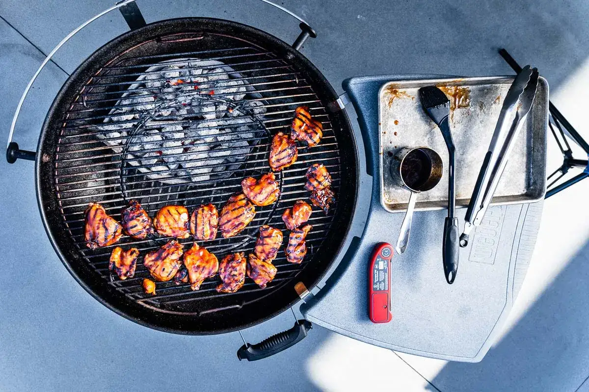 Grillad kyckling p&aring; en klotgrill b&auml;st i test, med tillbeh&ouml;r som pensel, t&aring;ng och termometer.
