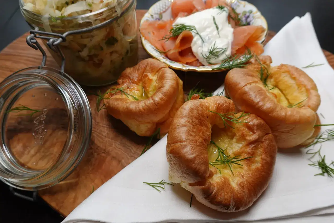Goldbraune Yorkshire Pudding-Törtchen mit Dill garniert, daneben Lachs mit Frischkäse und ein Glas Krautsalat.