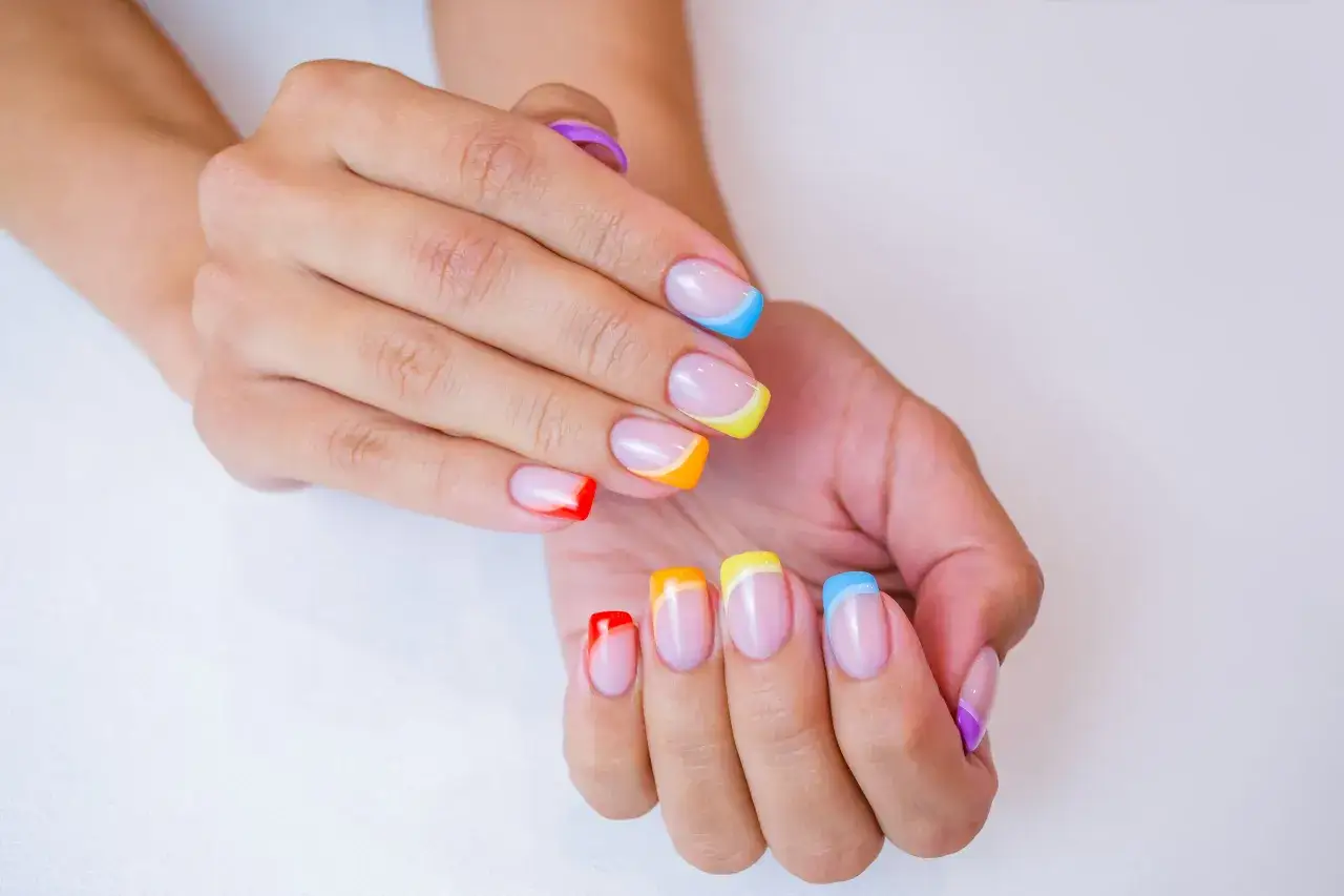 Kolorowe paznokcie na lato: francuski manicure w odcieniach tęczy, od czerwieni po fiolet.