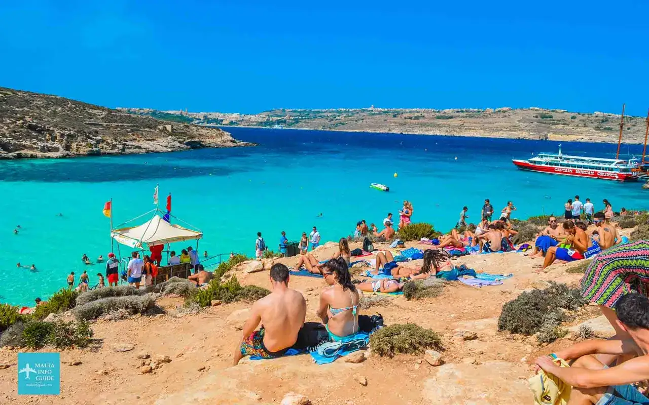 Sonniges Malta im Oktober: Menschen entspannen am Strand, baden im t&uuml;rkisfarbenen Meer. Ein Boot ankert vor der K&uuml;ste.