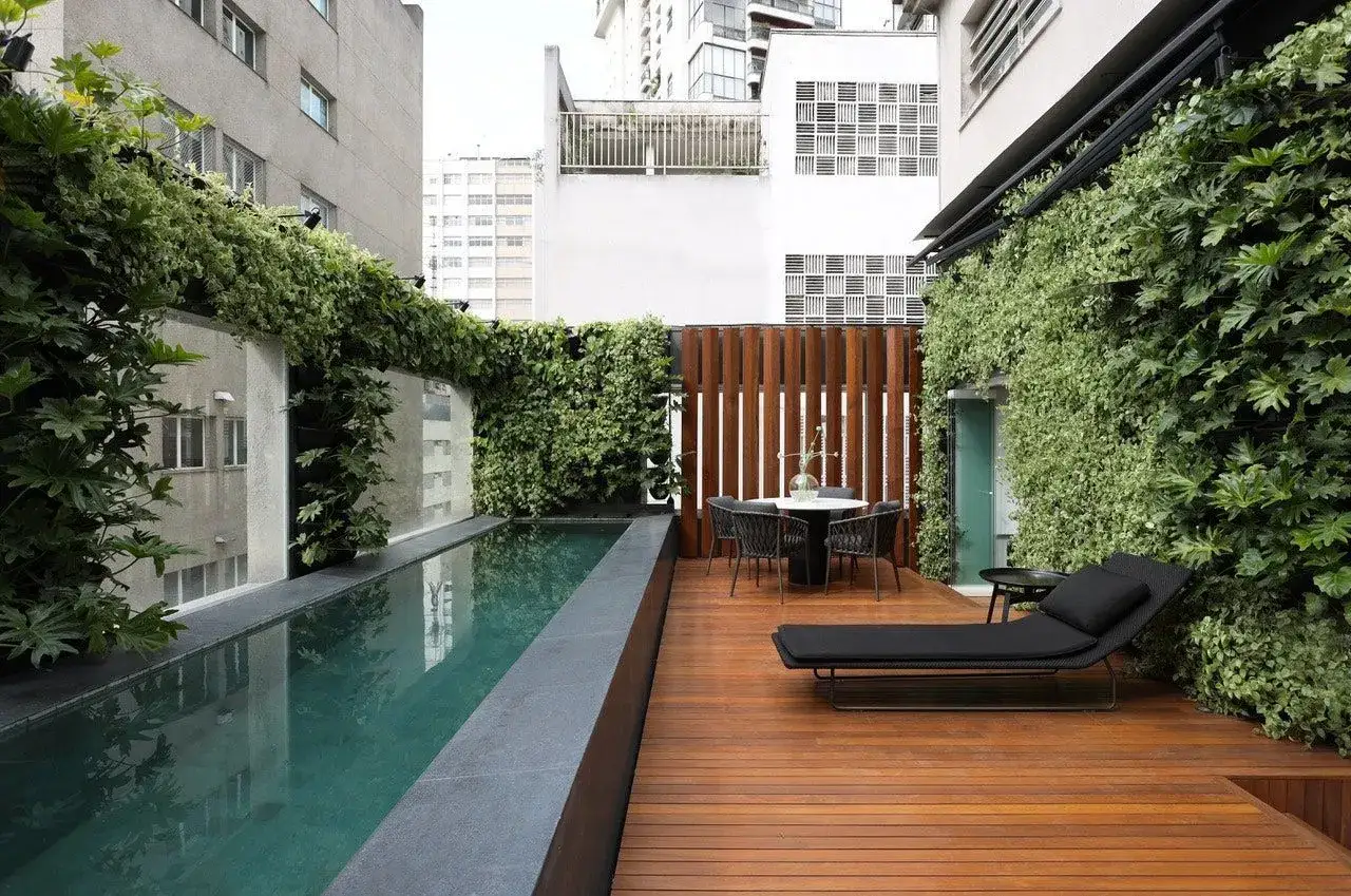 Une piscine et une terrasse en bois avec une décoration luxuriante autour de la piscine, créant un oasis urbain.