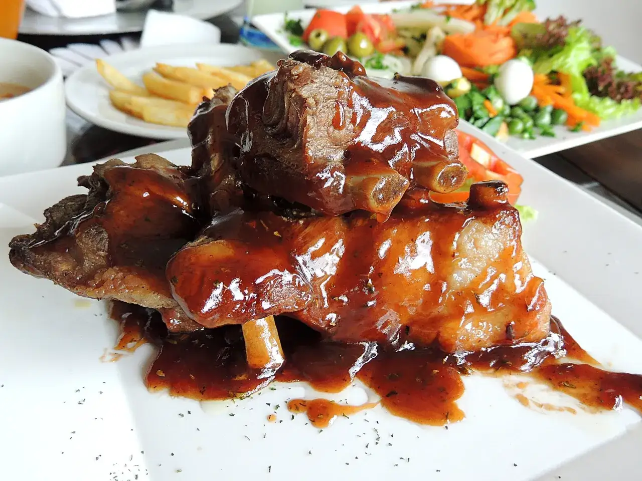 Délicieux travers de porc nappés d'une sauce brune savoureuse, servis sur une assiette blanche.