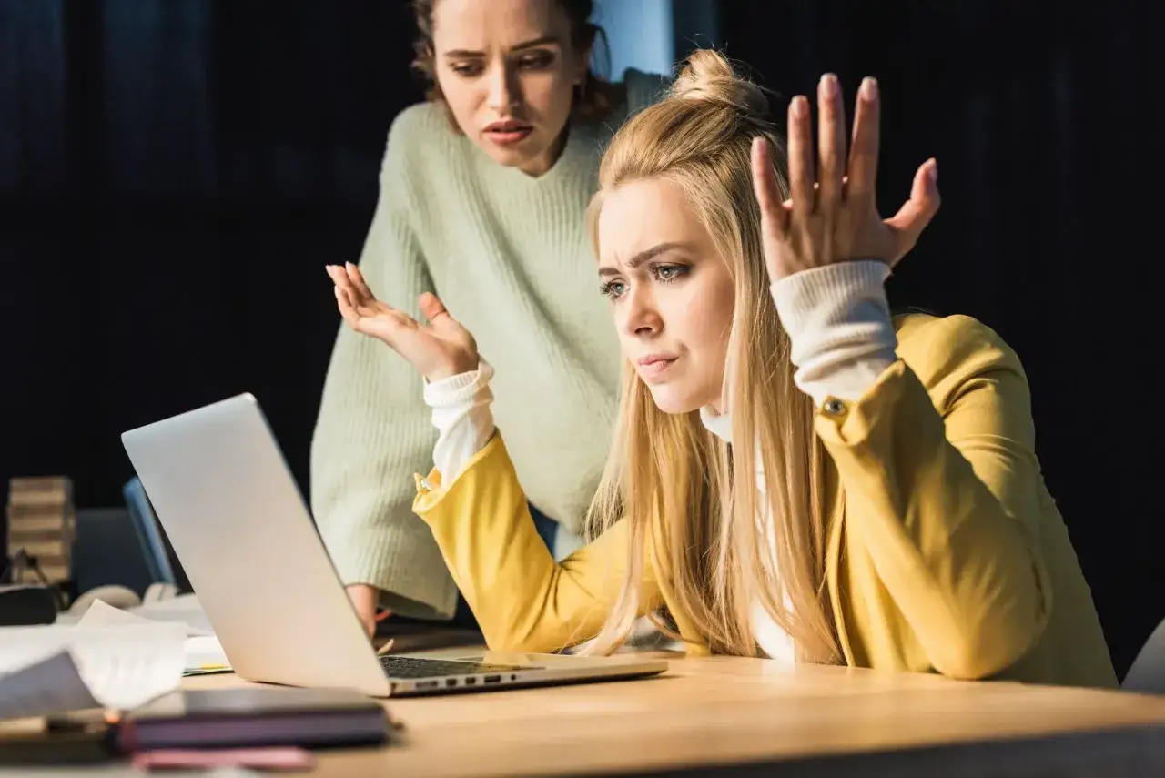 Dwie kobiety patrzą na laptopa z niedowierzaniem. Jedna z nich gestykuluje, jakby broniła się przed zniesławieniem.