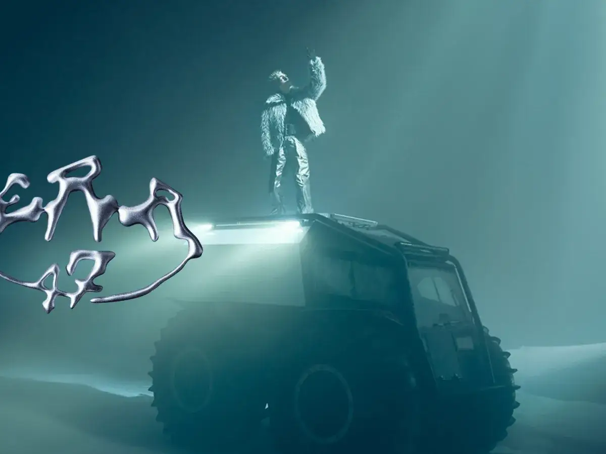Oki 47, o co chodzi? Artysta w futrzanym płaszczu na pojeździe terenowym w mglistym krajobrazie.