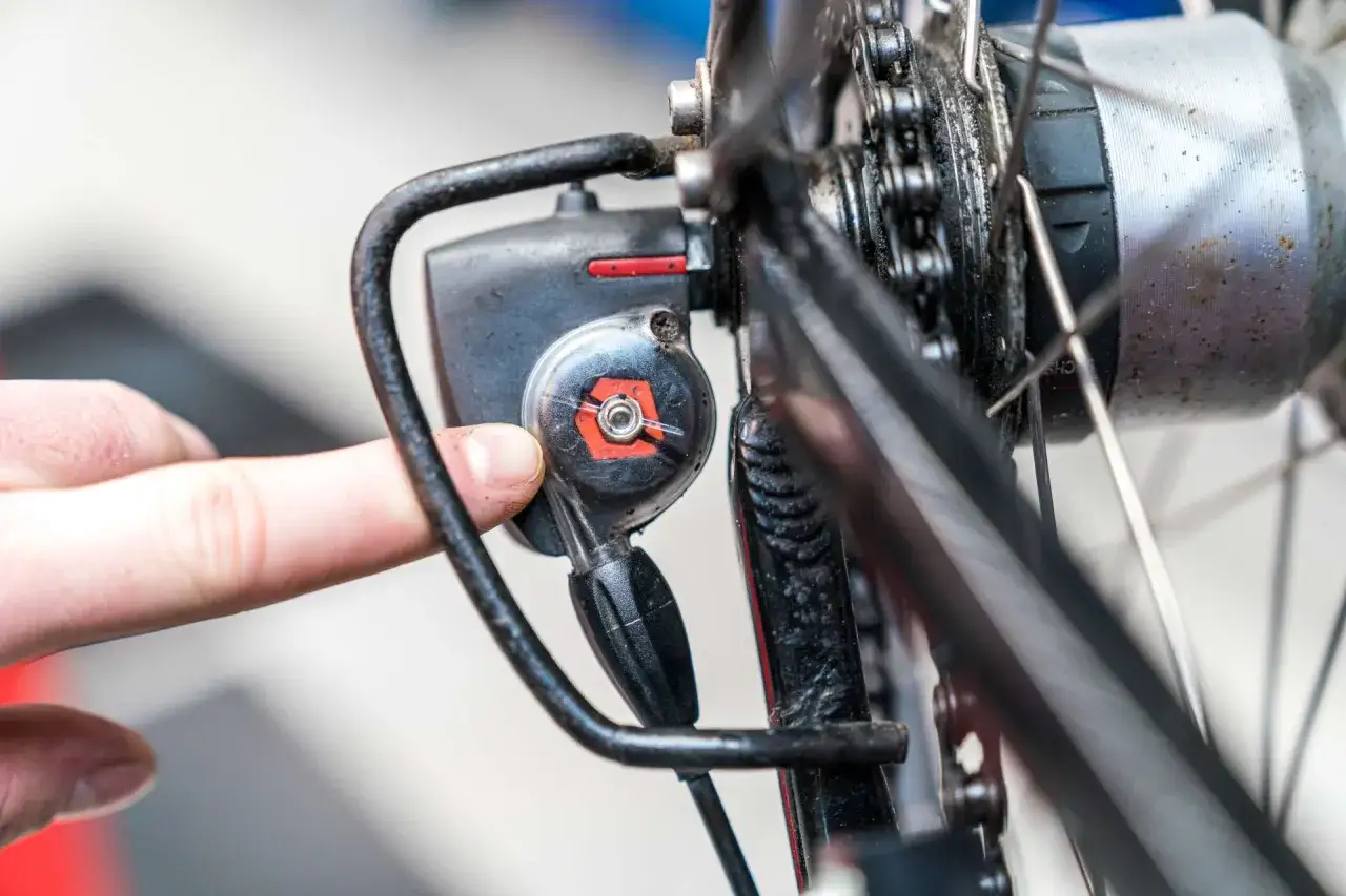 Finger dreht an der Einstellschraube, um die Nabenschaltung einzustellen. Nahaufnahme des Fahrradteils.